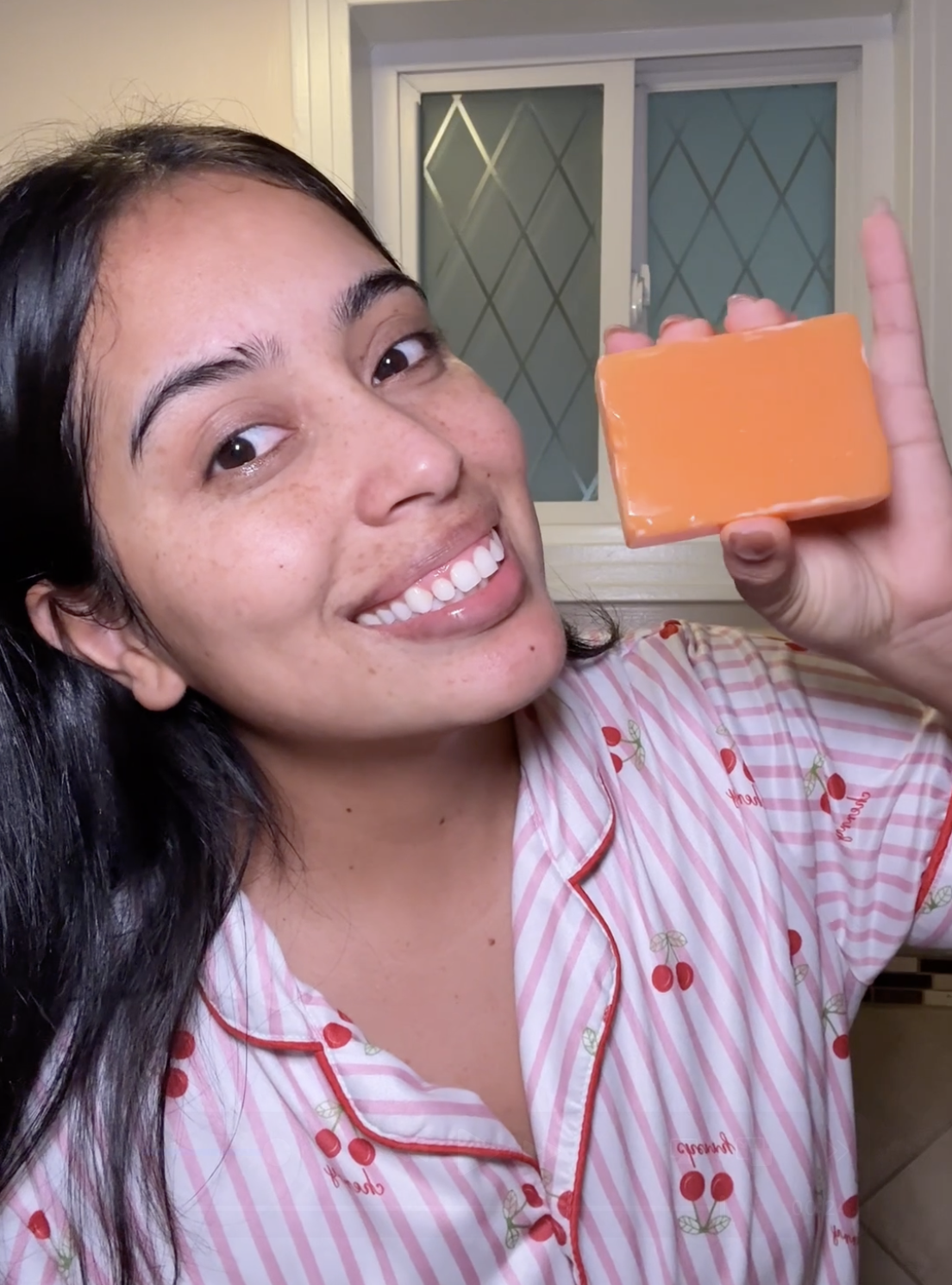 Person in striped pajamas holding an orange soap bar, smiling indoors.