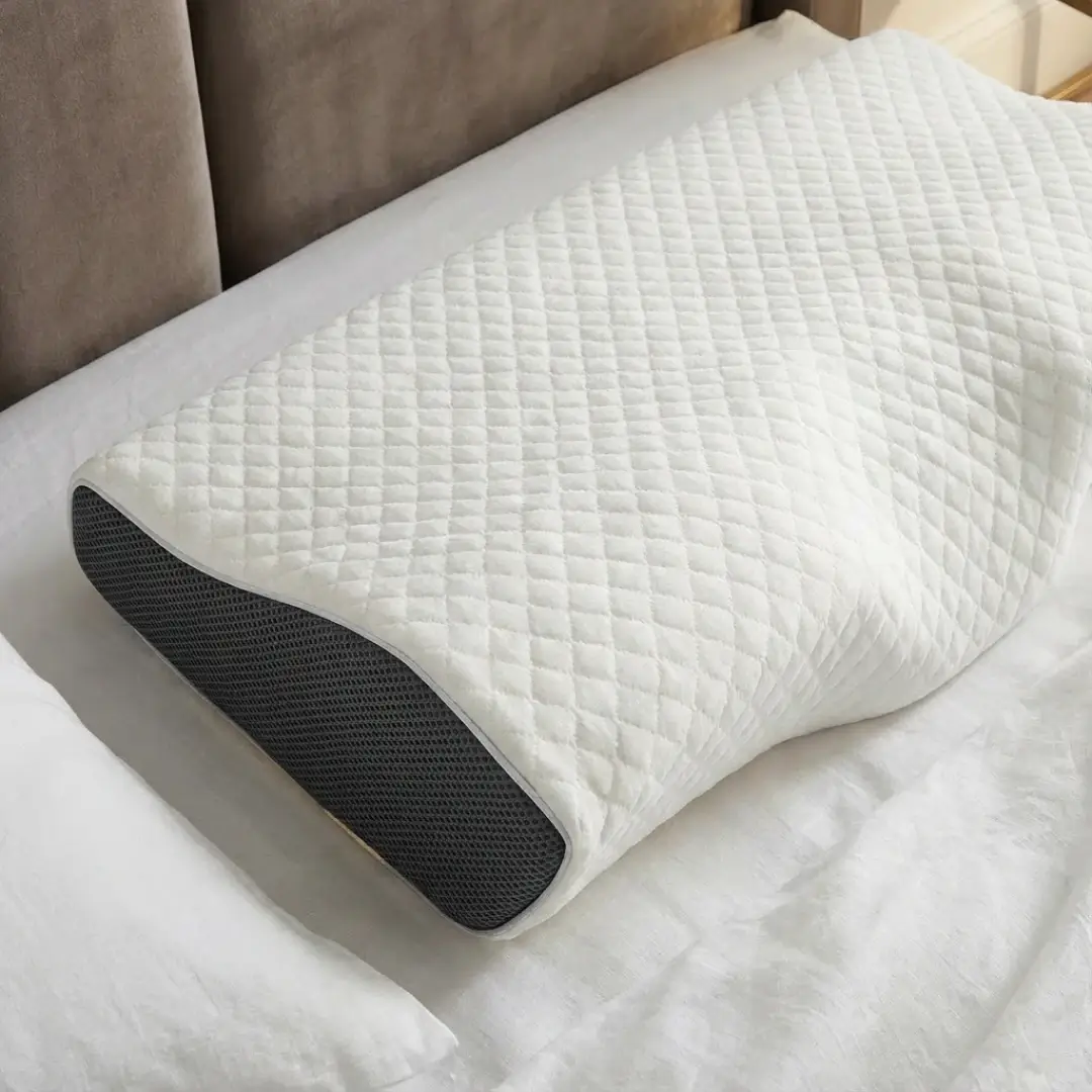 A contoured pillow with a white quilted top and gray mesh sides resting on a bed.