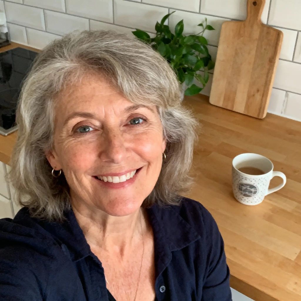 Smiling person in a kitchen with a plant, mug, and cutting board on the counter.