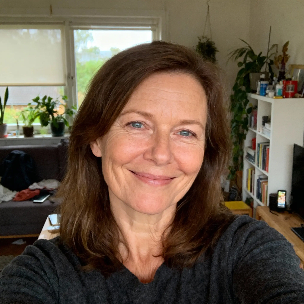 Person smiling in a room with plants and bookshelves in the background.