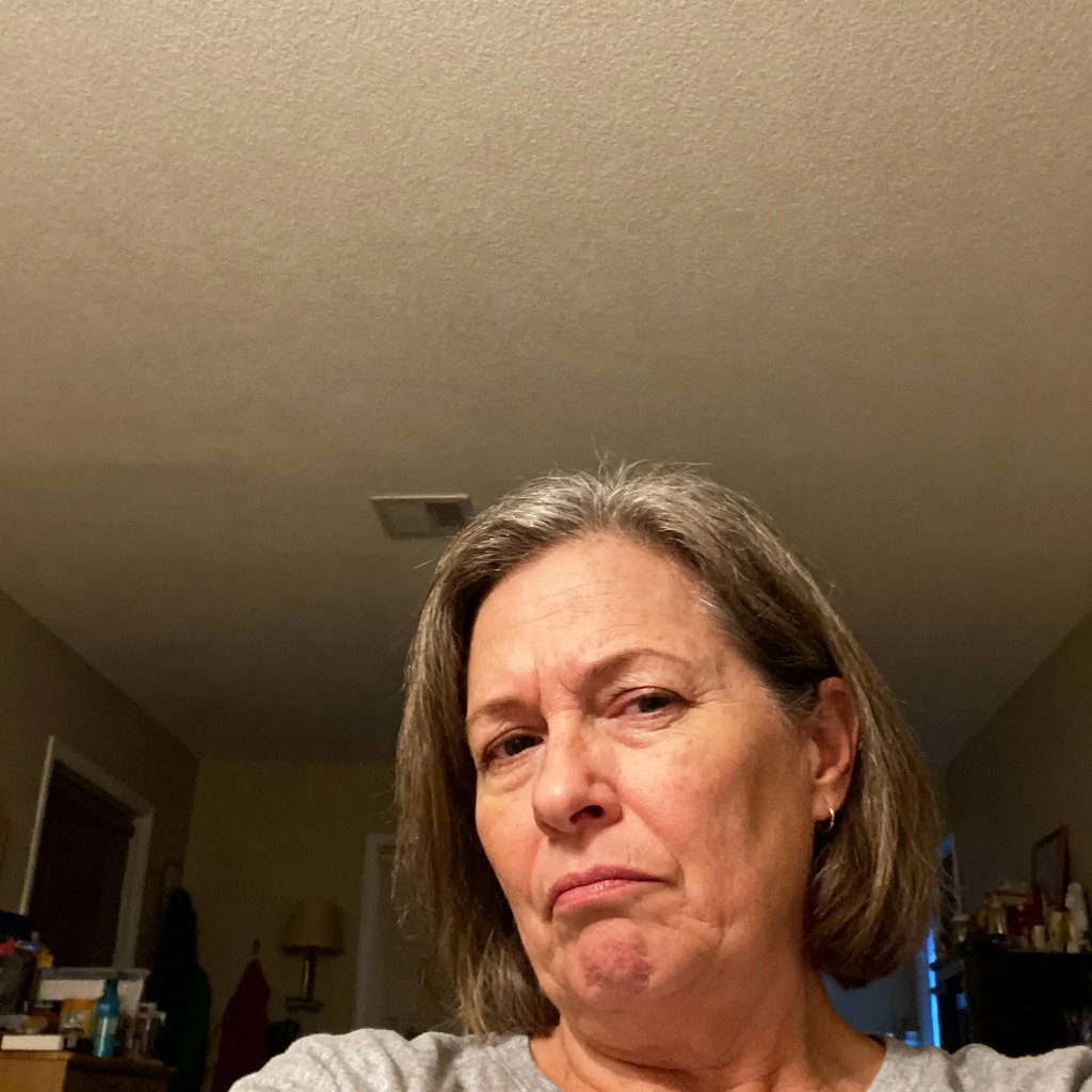 A person with short hair looking into the camera in a dimly lit room.