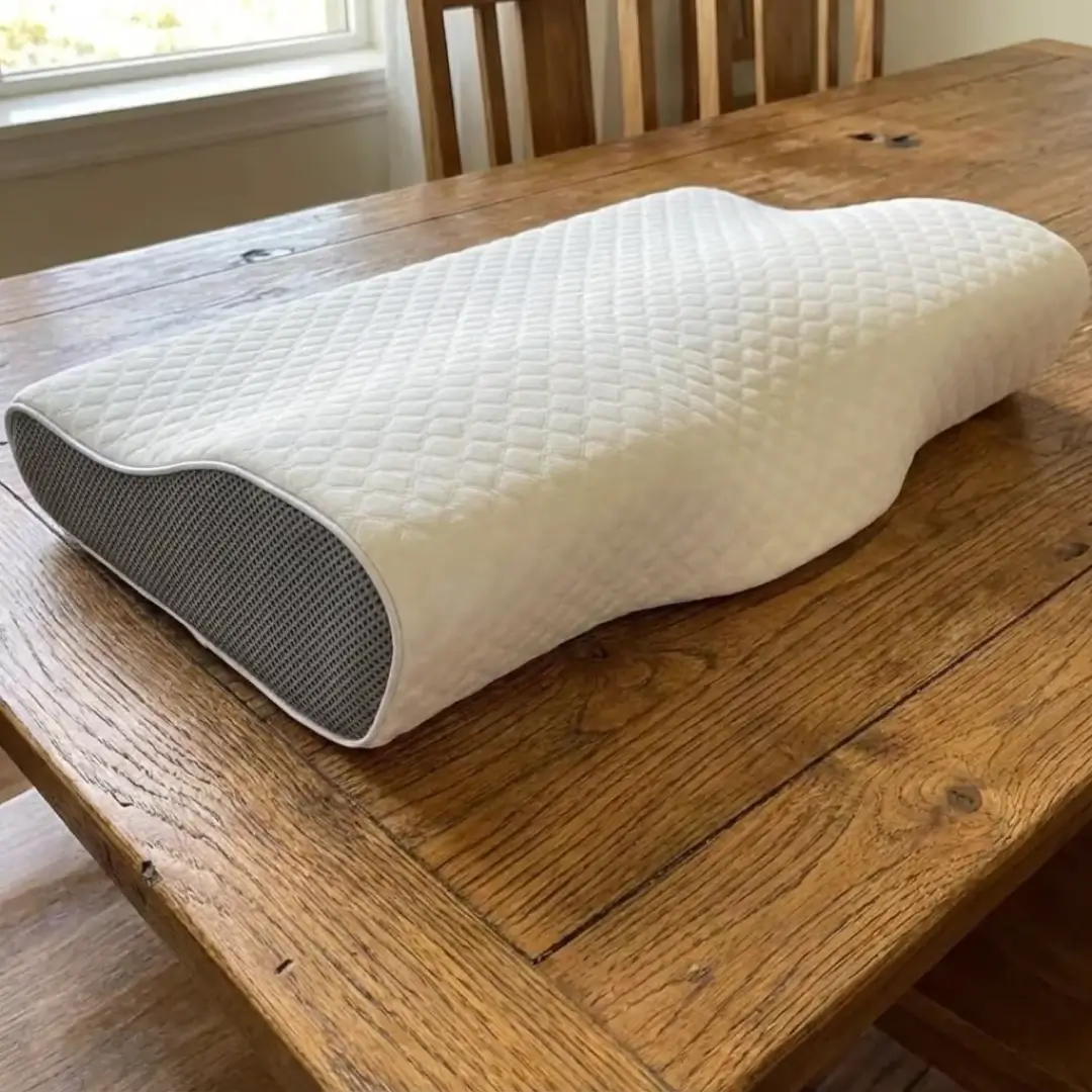A white contoured pillow with grey mesh sides resting on a wooden table.