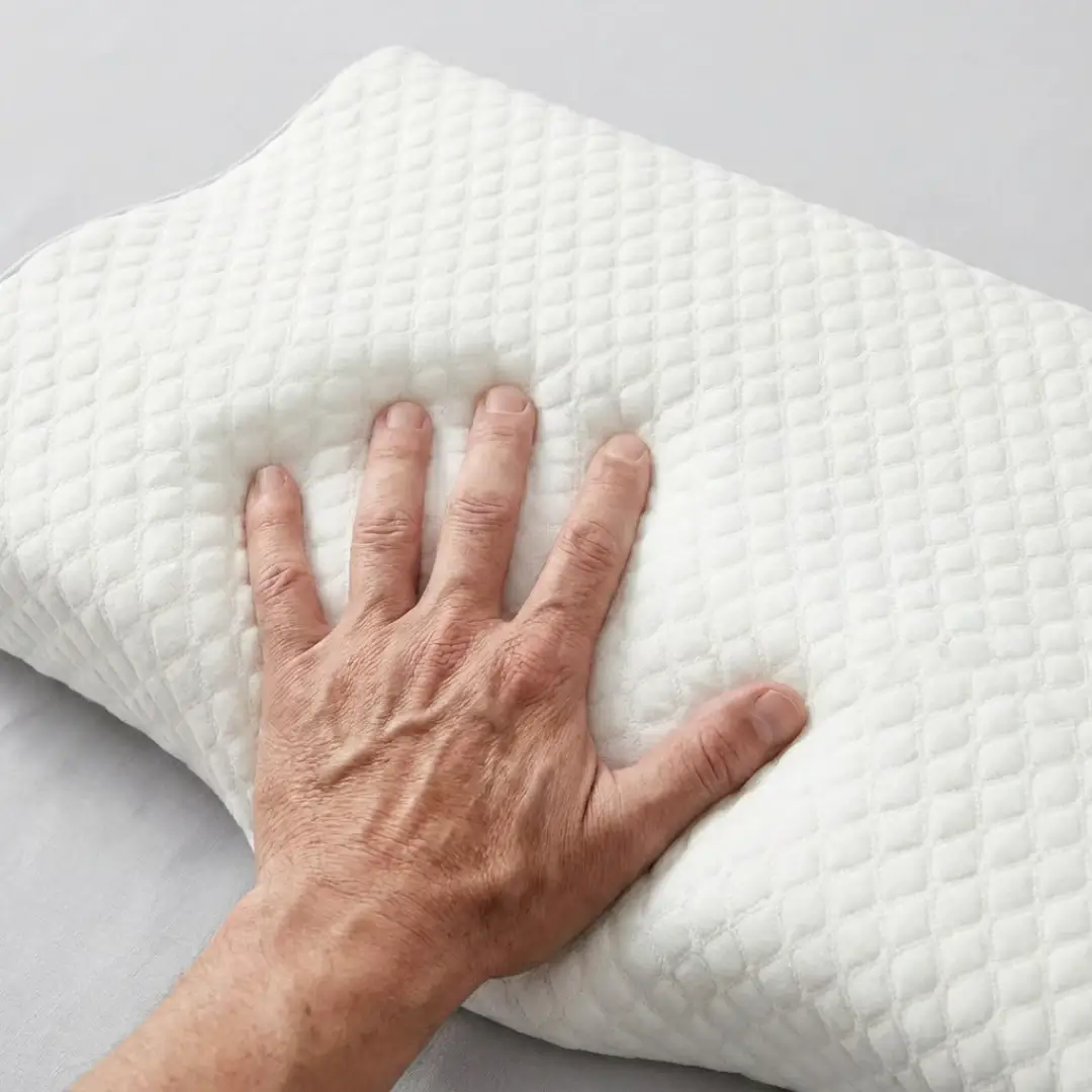 A person's hand pressing down on a white, quilted pillow, creating an indentation.