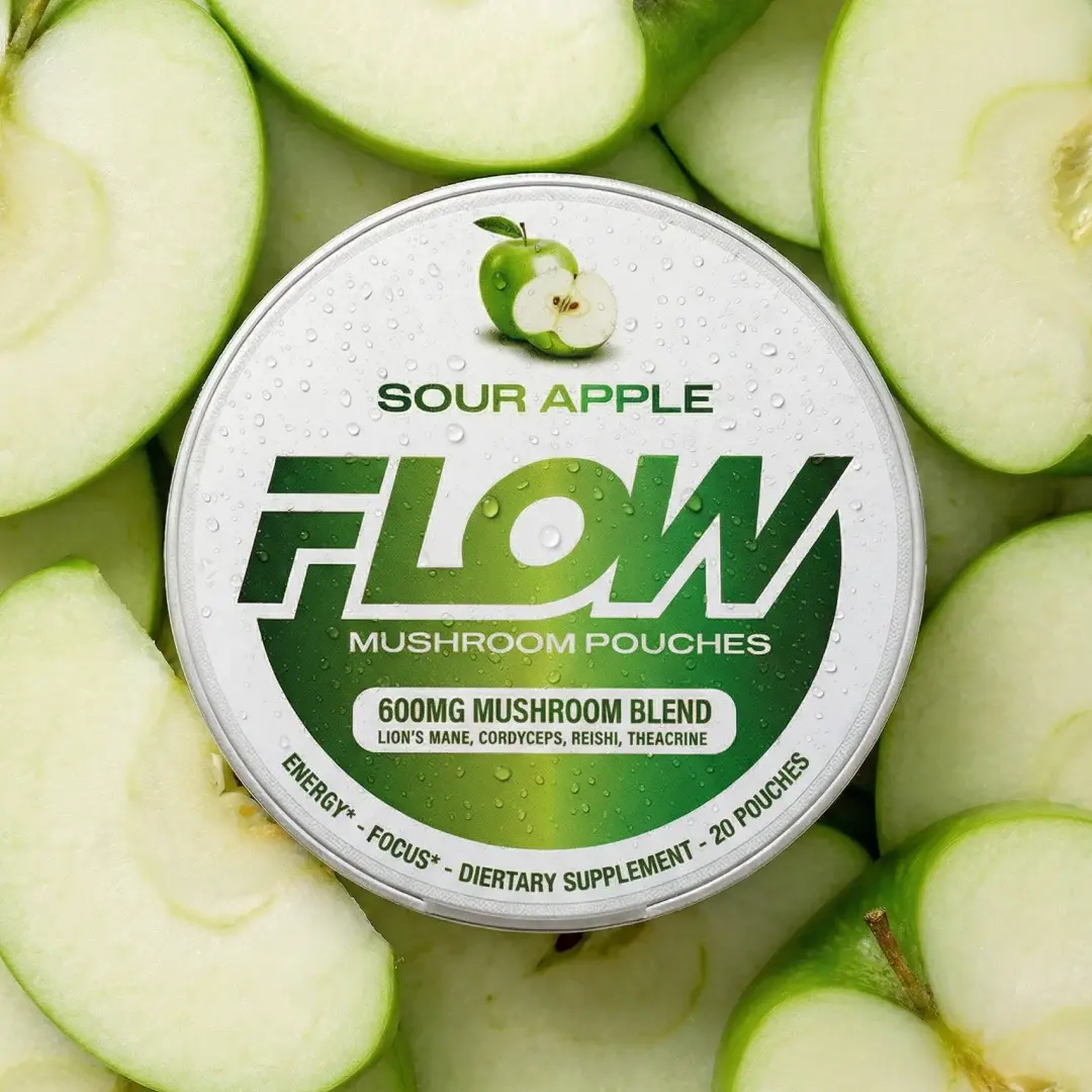A circular tin of Flow Sour Apple Mushroom Pouches sitting on a bed of sliced green apples.