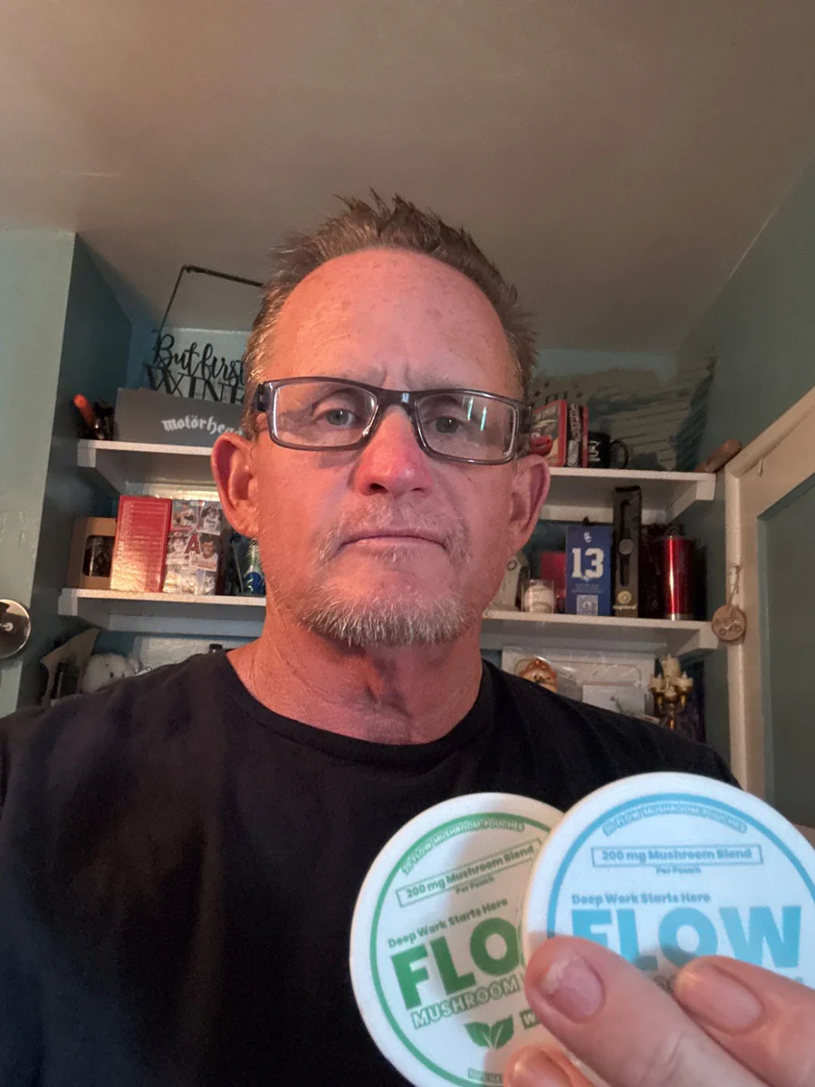 A man in glasses holds two circular white containers labeled 'FLOW' toward the camera.