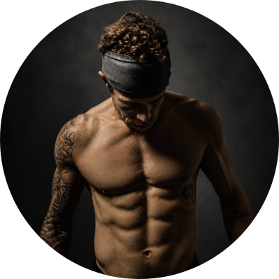 A circular portrait of a shirtless, muscular man with tattoos on his arm, looking down.