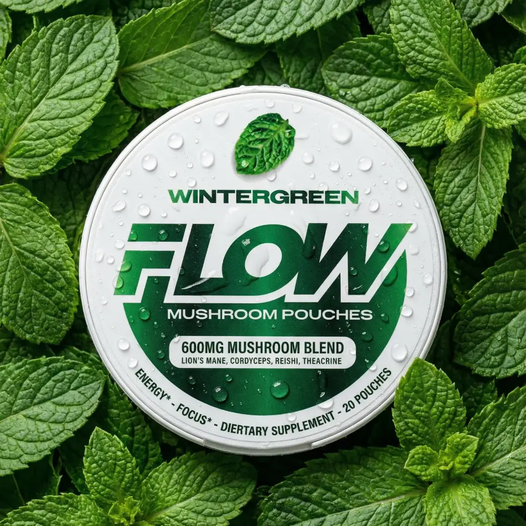 A white circular tin of Wintergreen Flow Mushroom Pouches resting on a bed of fresh mint leaves.