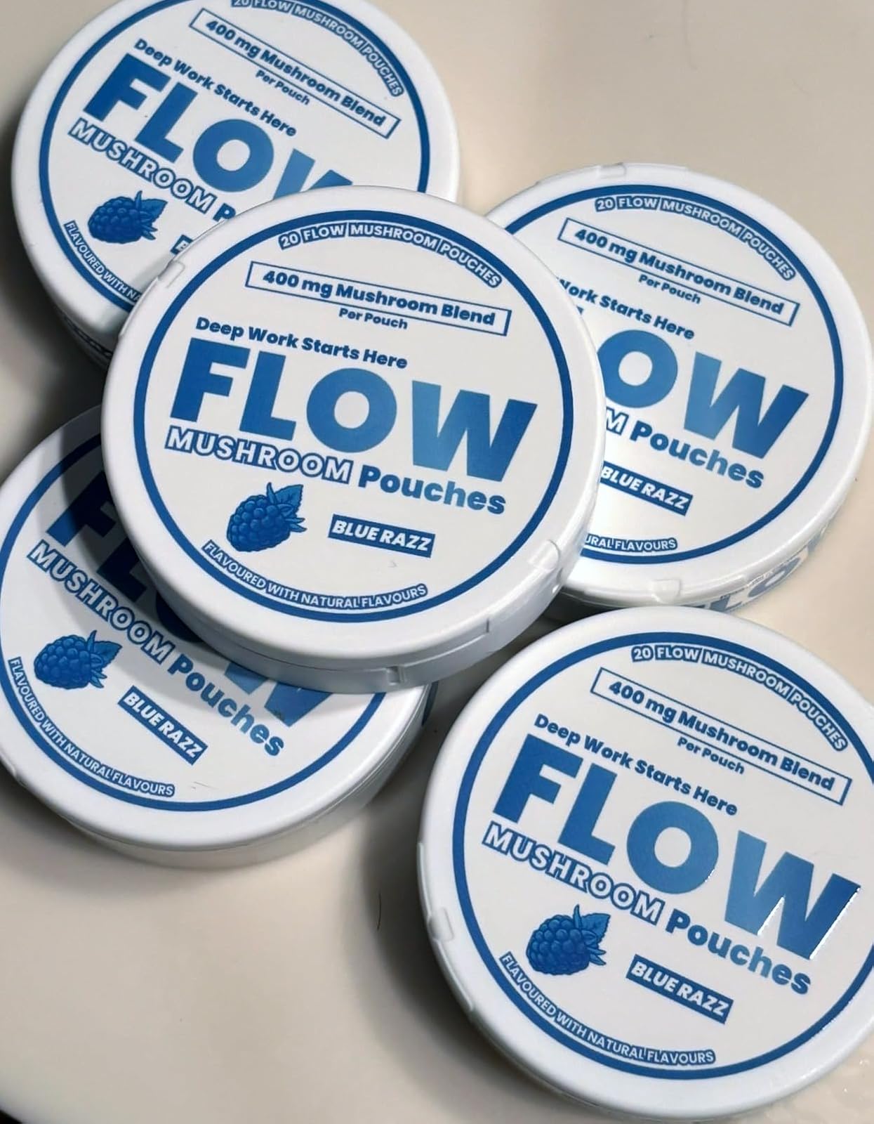 Several white, circular containers of Flow Mushroom Pouches in the Blue Razz flavor are scattered on a surface.
