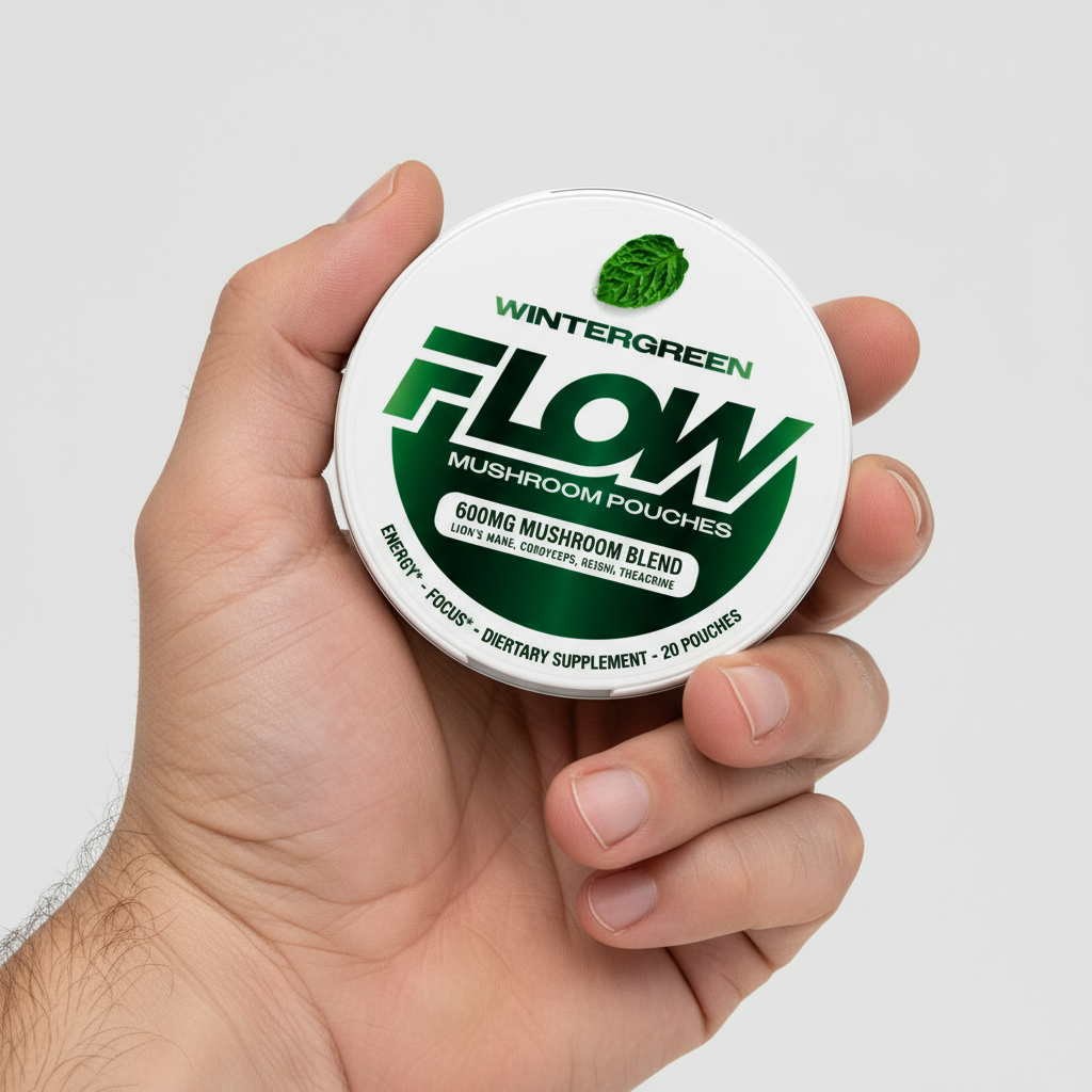 A hand holding a white, circular tin of Flow Wintergreen Mushroom Pouches against a white background.
