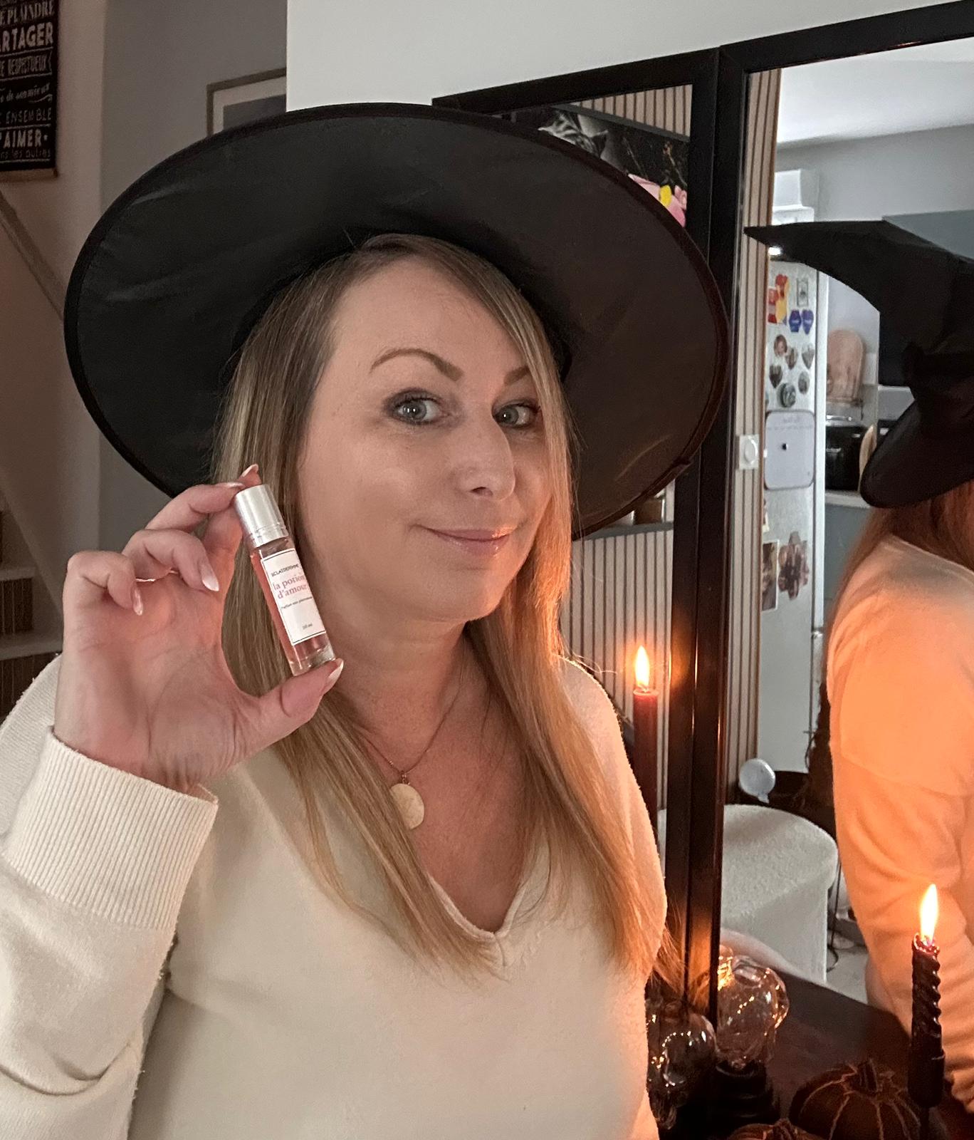 Woman in a witch hat holding a small bottle by candlelight.