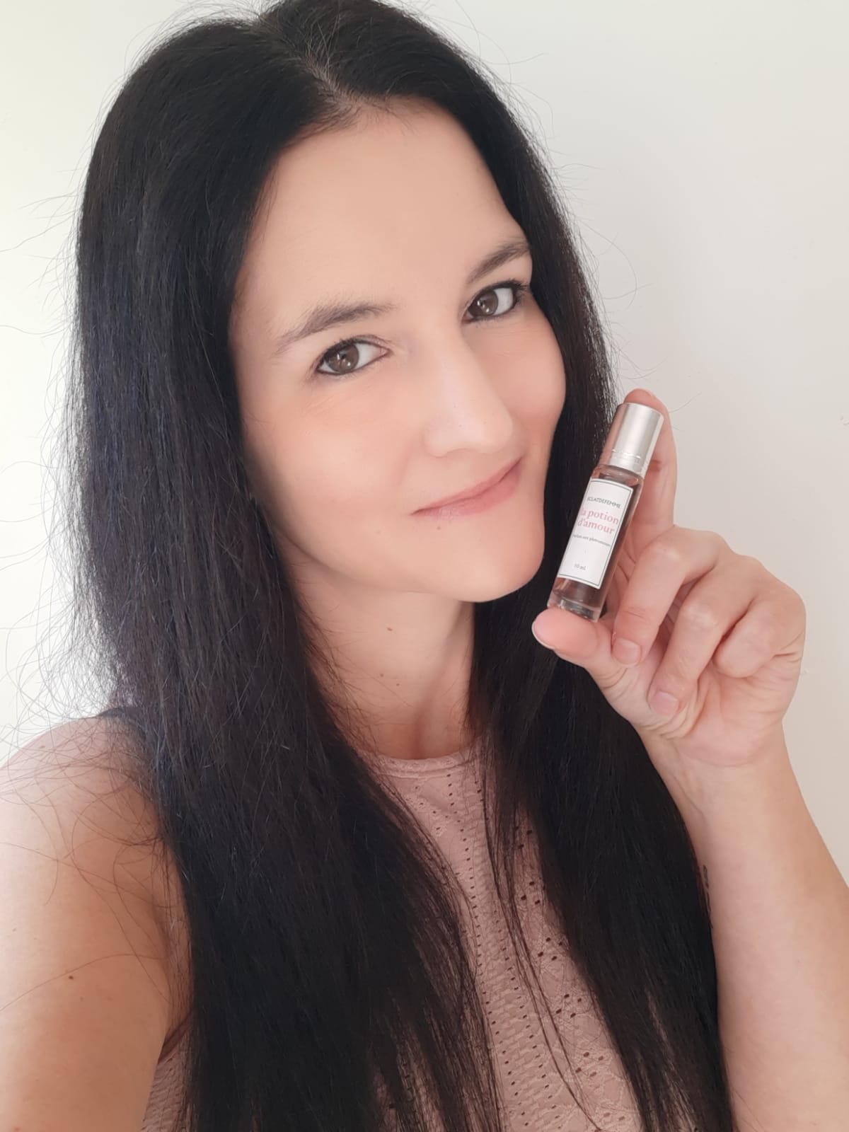 Person holding a small perfume bottle, smiling against a plain background.