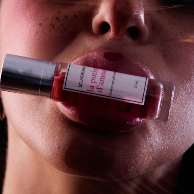 Close-up of lips holding a small perfume bottle.