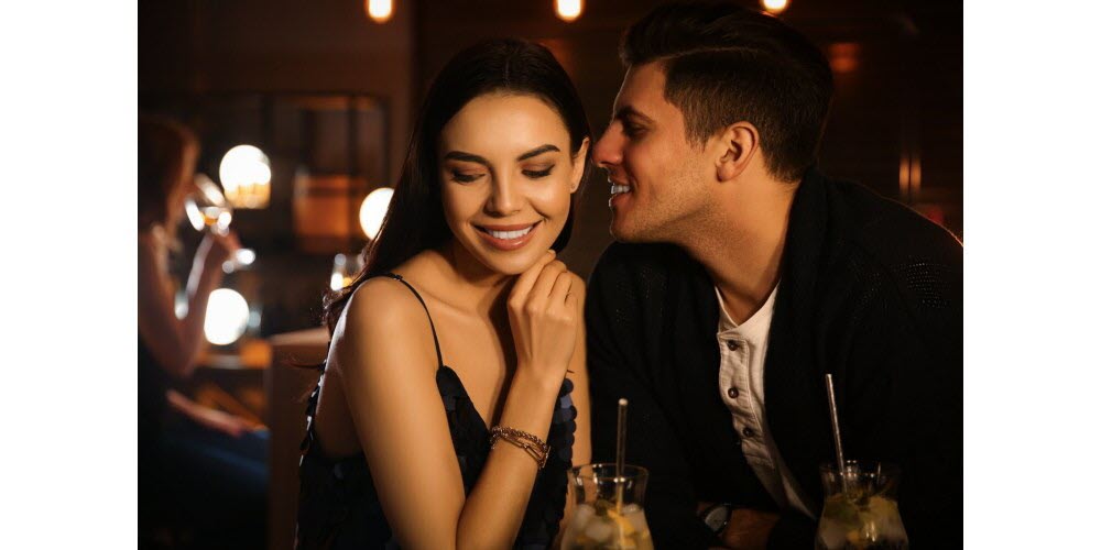 A couple smiling and talking at a dimly lit bar.