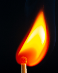 Close-up of a lit match with a bright flame against a dark background.