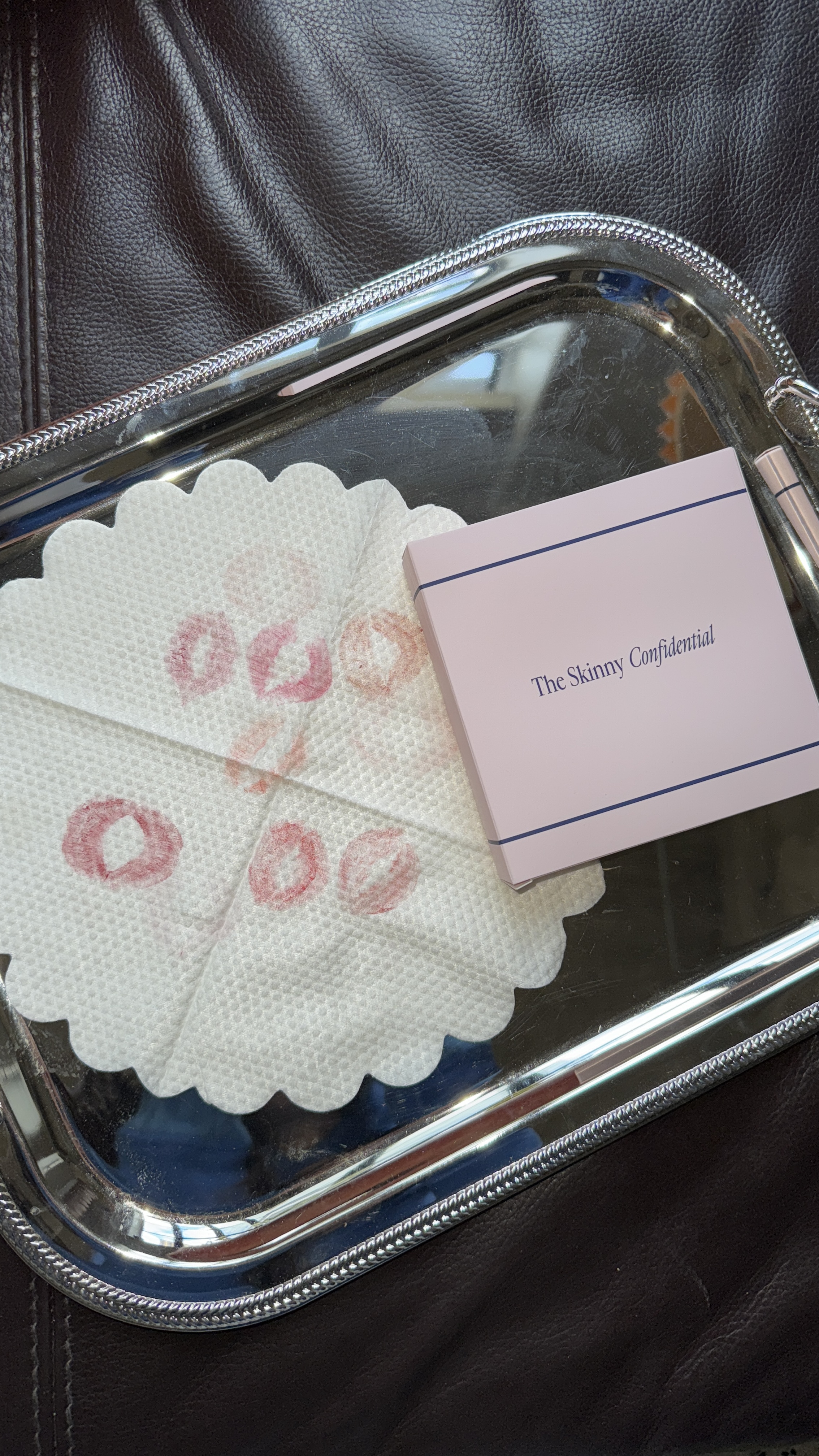 A silver tray holding a napkin with lipstick stains and a pink box labeled 'The Skinny Confidential'.