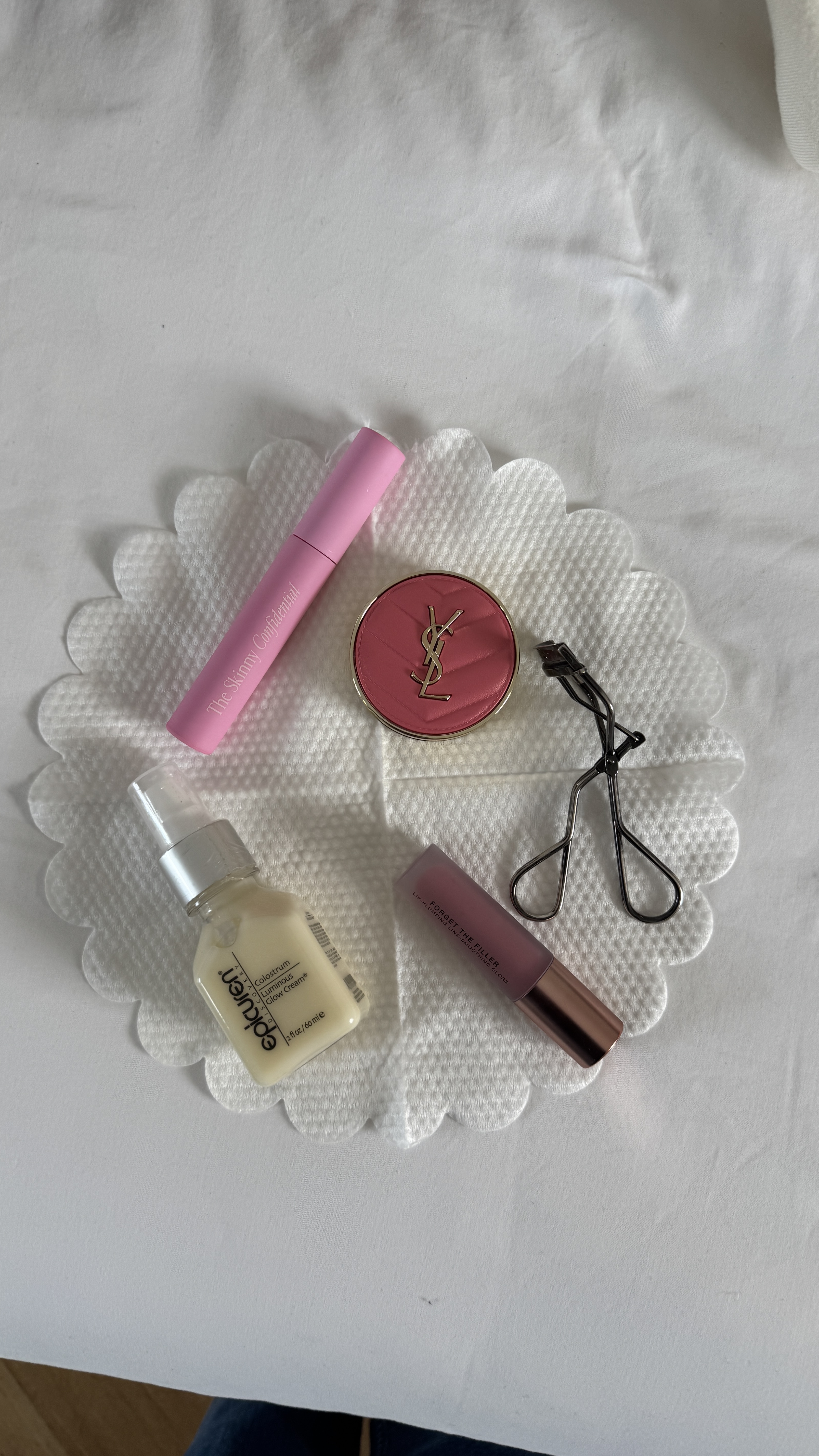 An overhead shot of various makeup and skincare items arranged on a white, scalloped cotton pad.