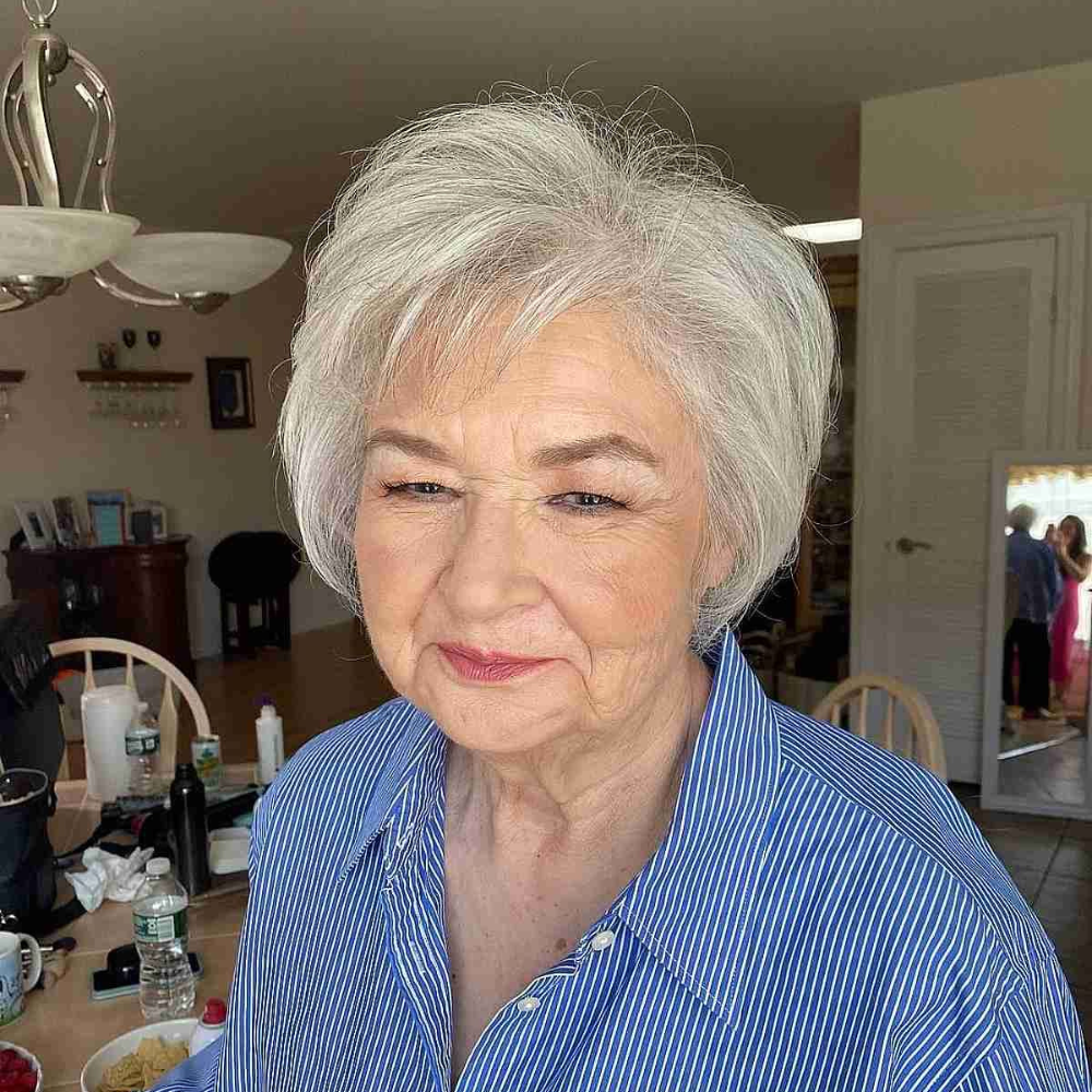 Elderly woman in a blue striped shirt sitting at a kitchen table.