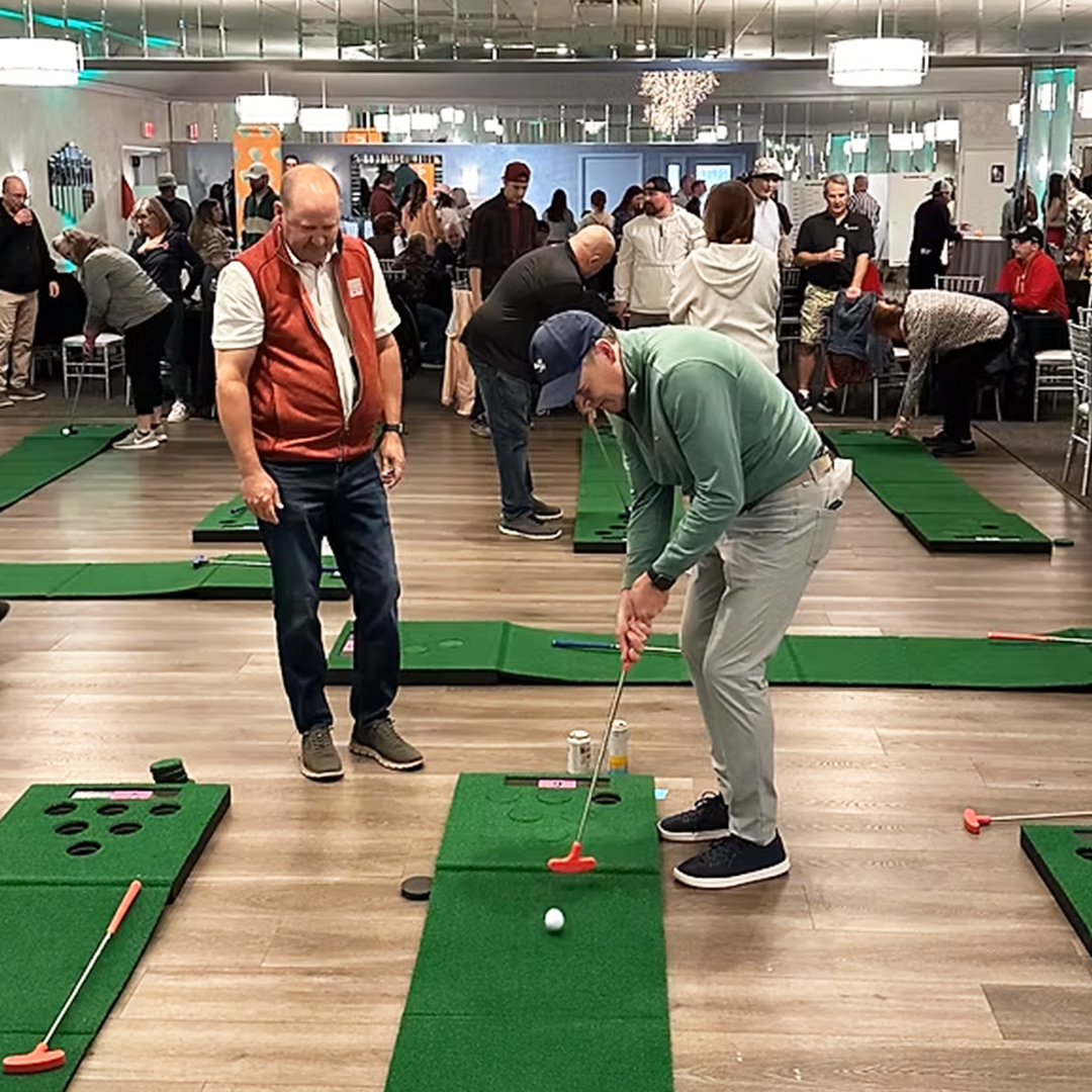 Indoor mini-golf event with people playing on green putting mats.