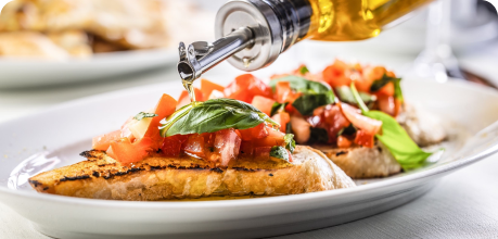 Bruschetta with tomatoes and basil being drizzled with olive oil on a white plate.