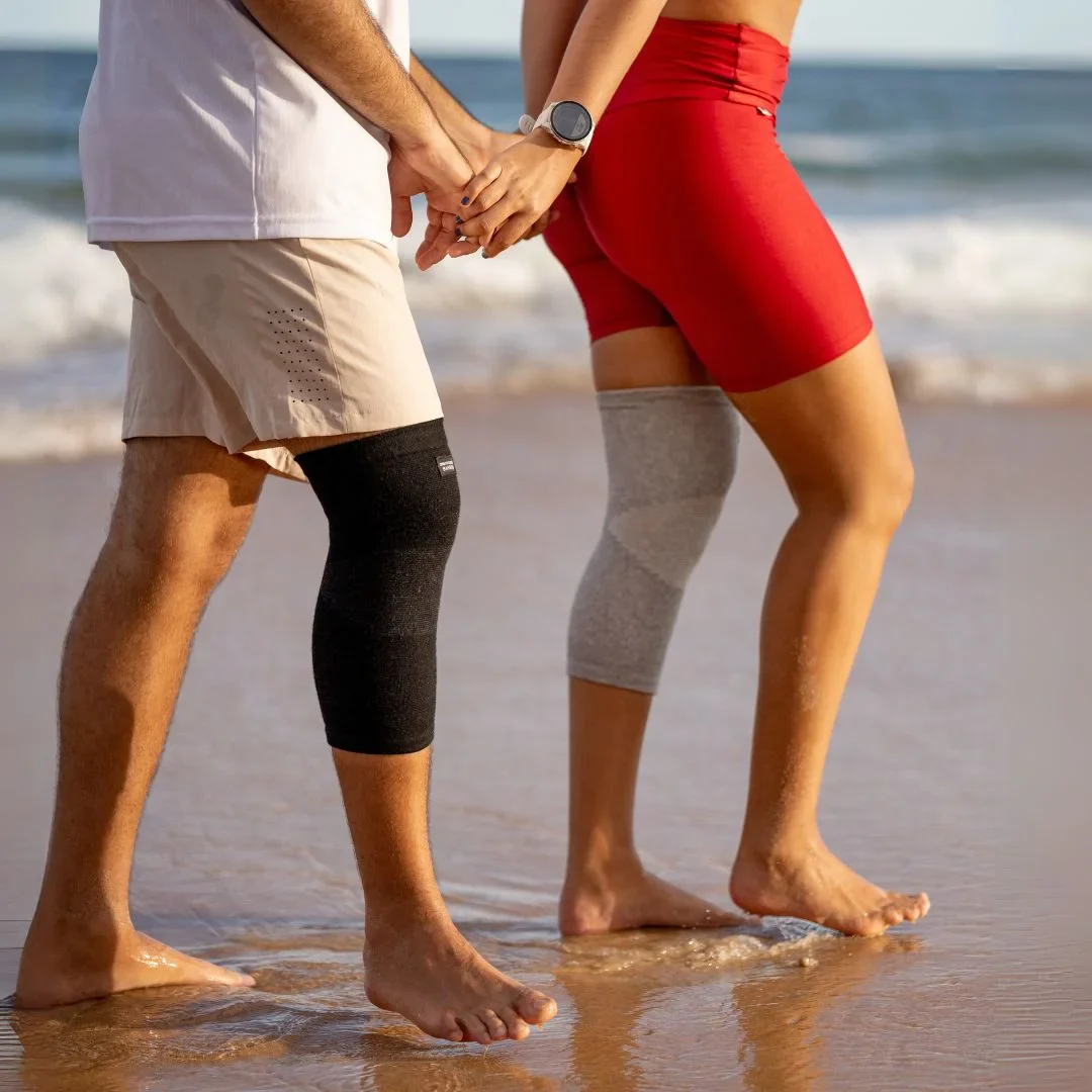 Two people walking on a beach with knee supports.