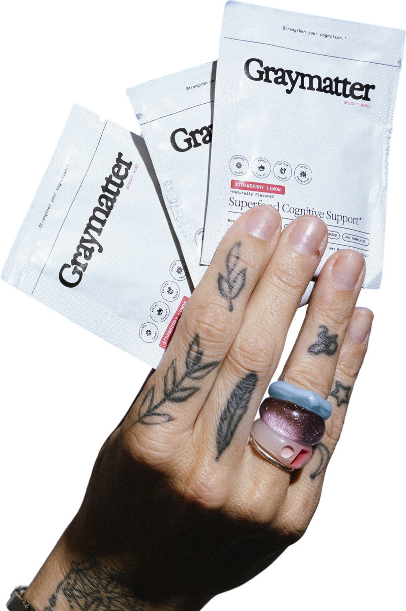 Tattooed hand holding packets labeled 'Graymatter' with rings on fingers.