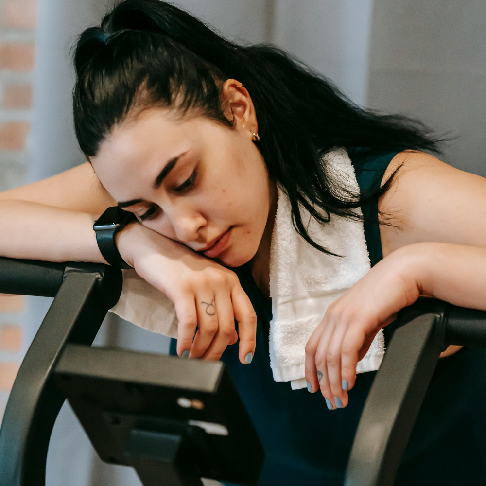 Woman resting on exercise equipment with a towel around her neck.
