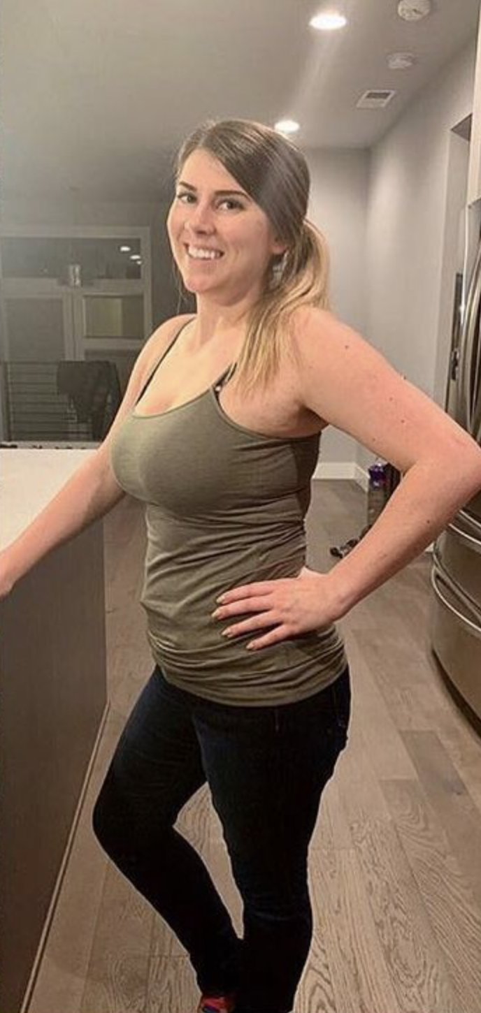 Person smiling and posing indoors with hands on hips, wearing casual clothes.