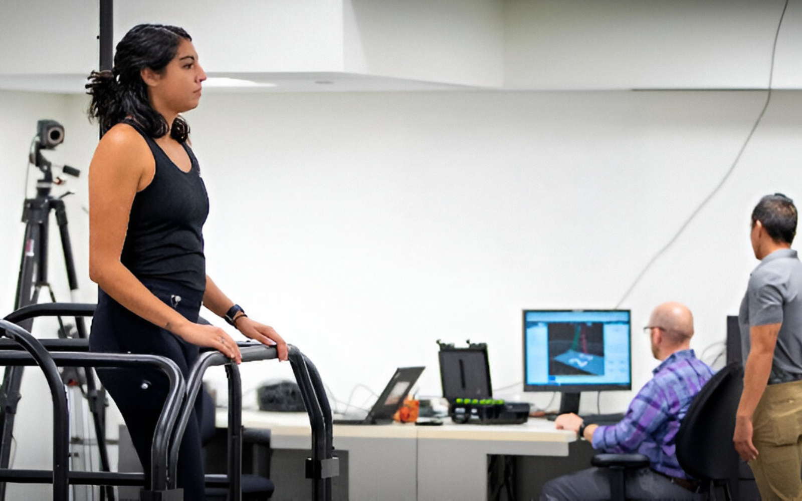 Person standing on a treadmill, with two people observing computer screens nearby.