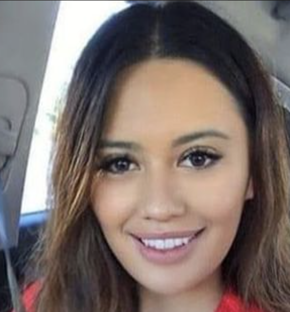A person smiling in a car, wearing a red top.