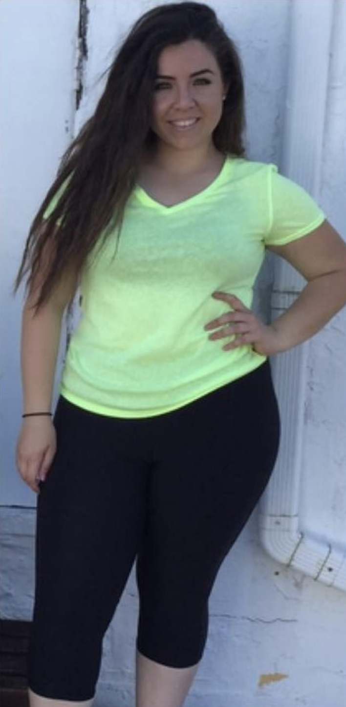Person wearing a neon yellow shirt and black leggings, standing against a white wall.