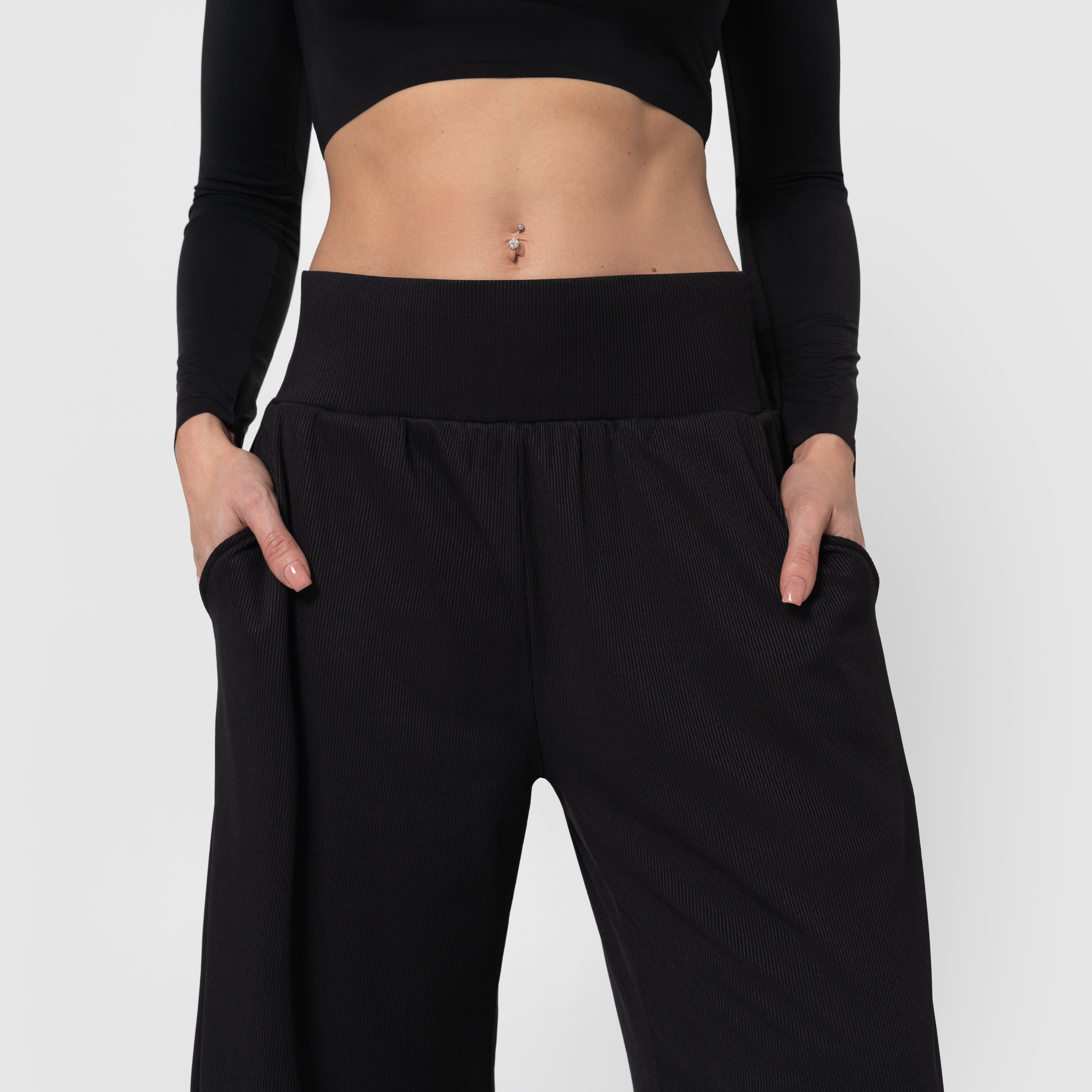 Person wearing a black crop top and high-waisted pants with hands in pockets.