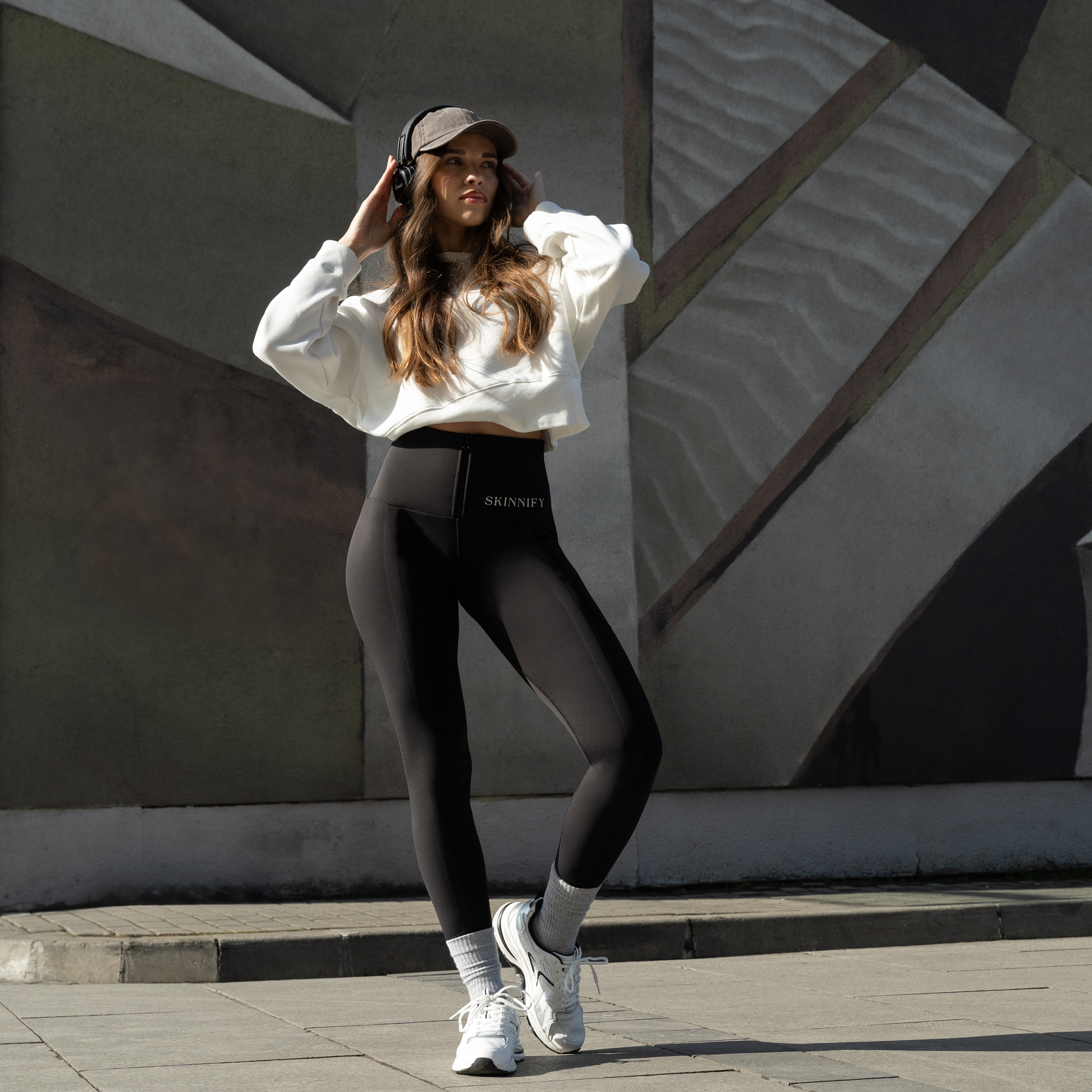 Woman in athletic wear and headphones standing against a geometric wall.
