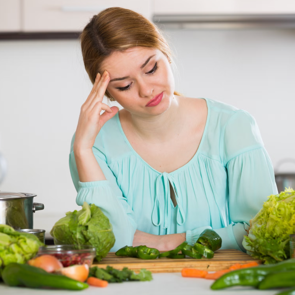 Woman in kitchen looking at vegetables with a thoughtful expression.