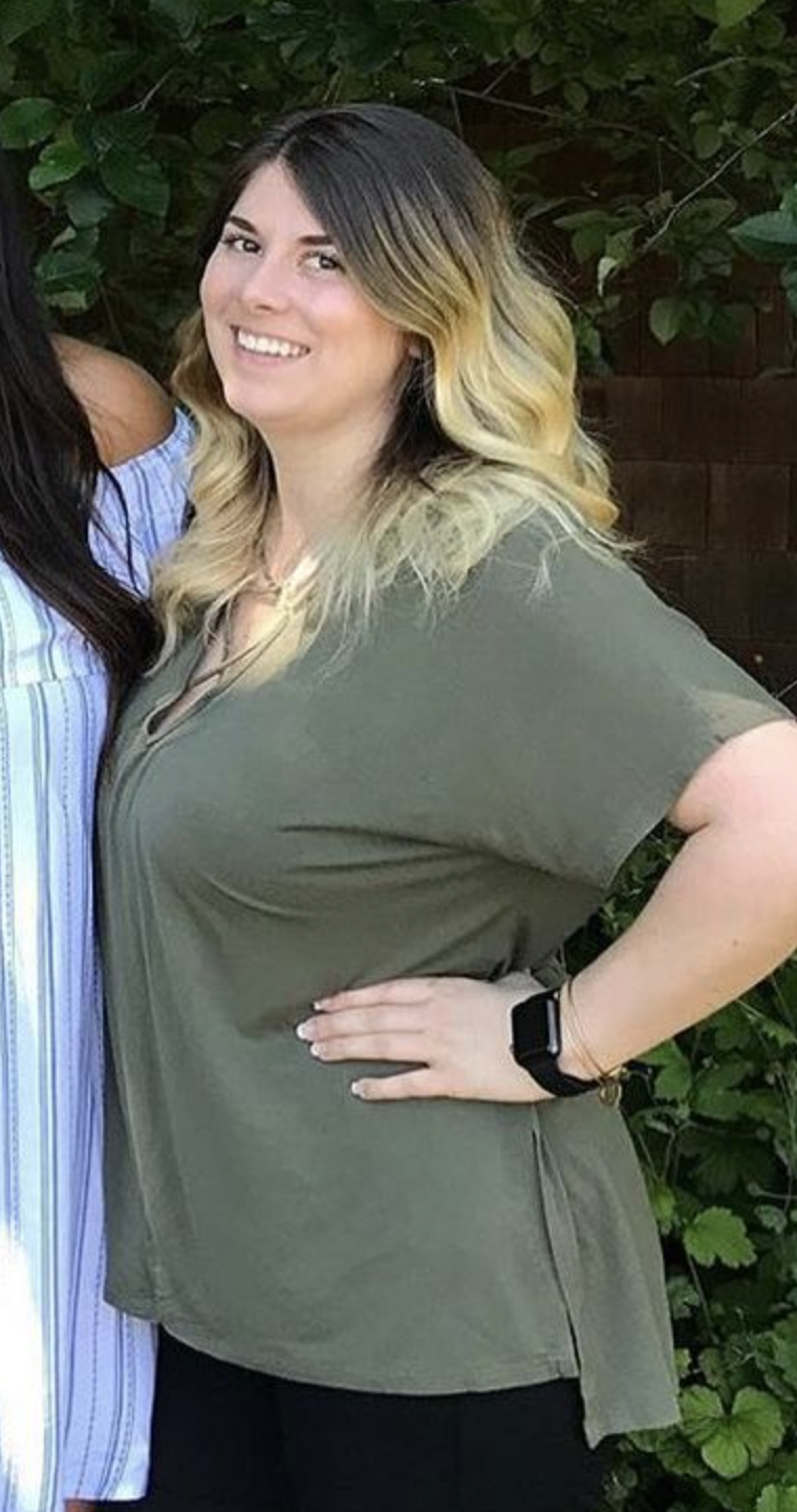 A person smiling outdoors, wearing an olive green shirt, with trees in the background.