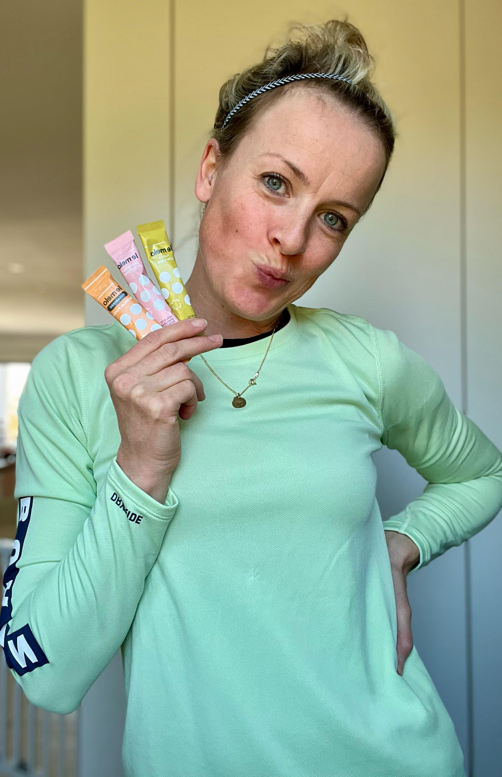 A person in a green top holds colorful skincare product tubes, striking a playful pose.