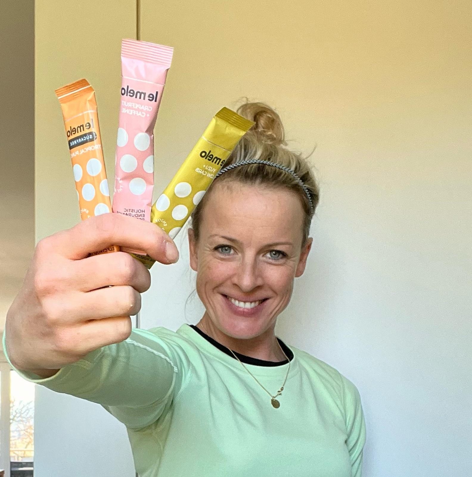 Person smiling, holding three colorful drink mix packets.
