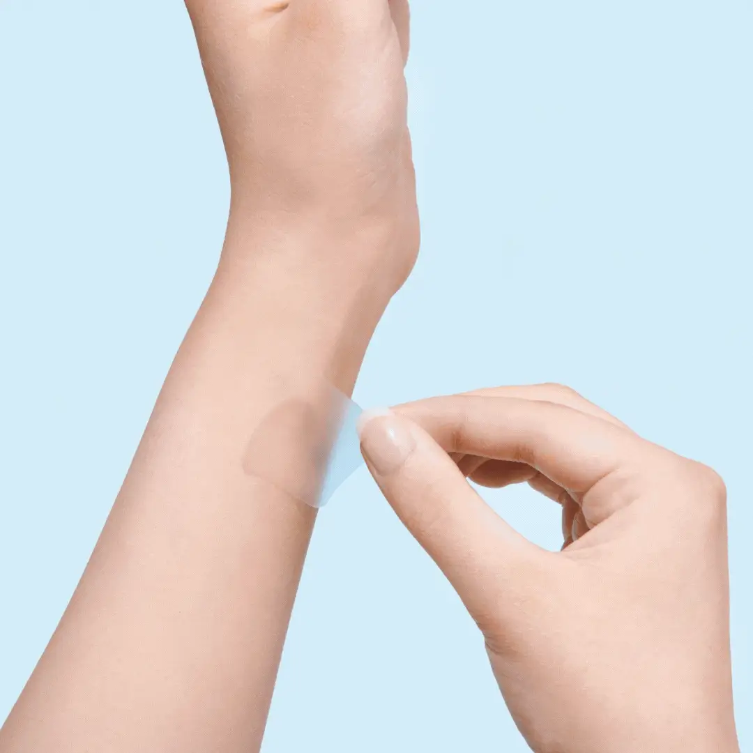 A person applying a transparent adhesive patch to their forearm.