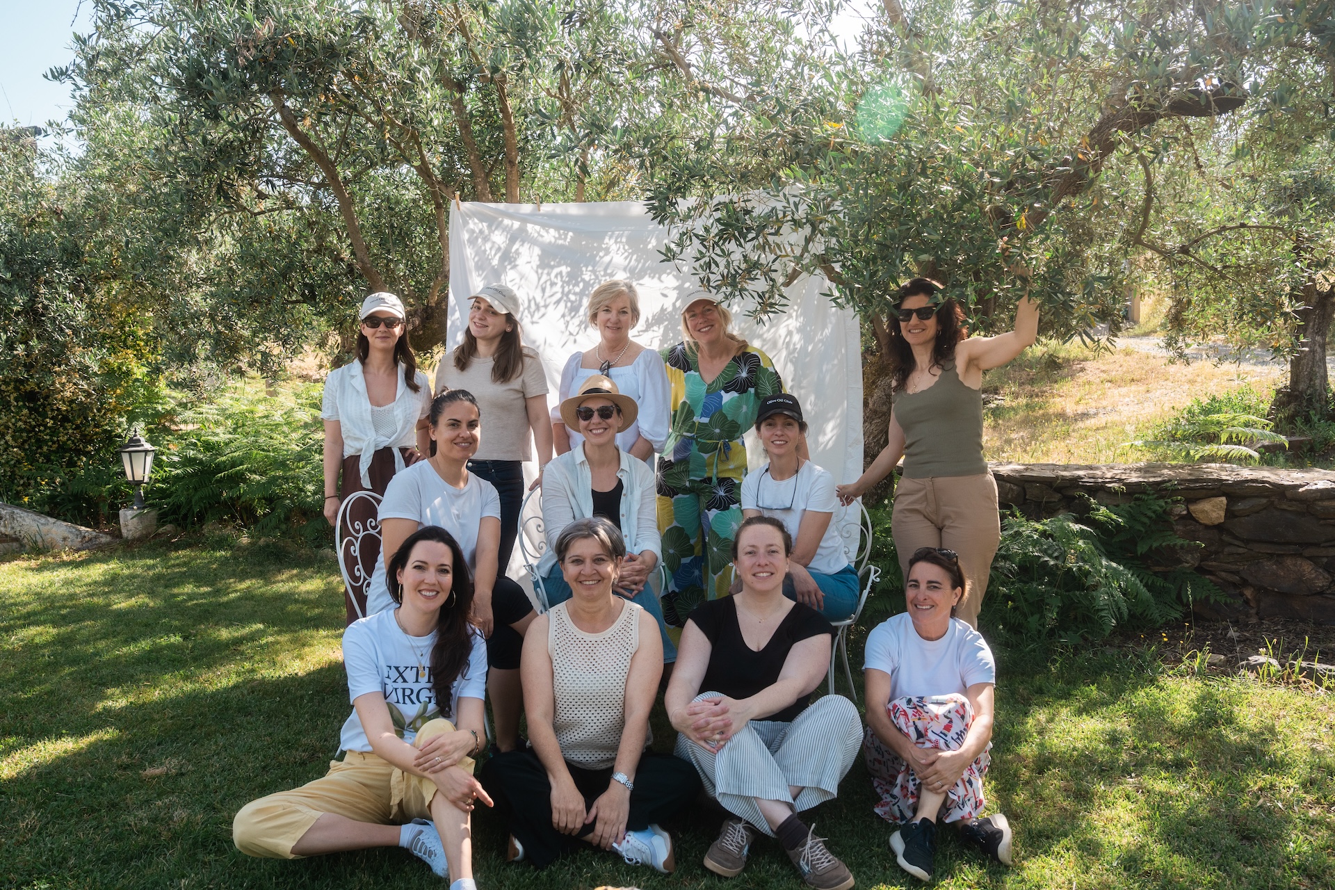 A group of twelve women pose for a photo outdoors in a garden on a sunny day.