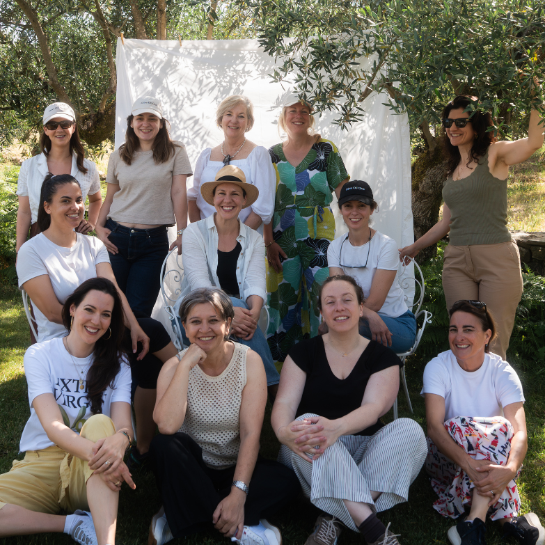 A group of twelve women posing for a photograph outdoors in a sunny, grassy area with trees.