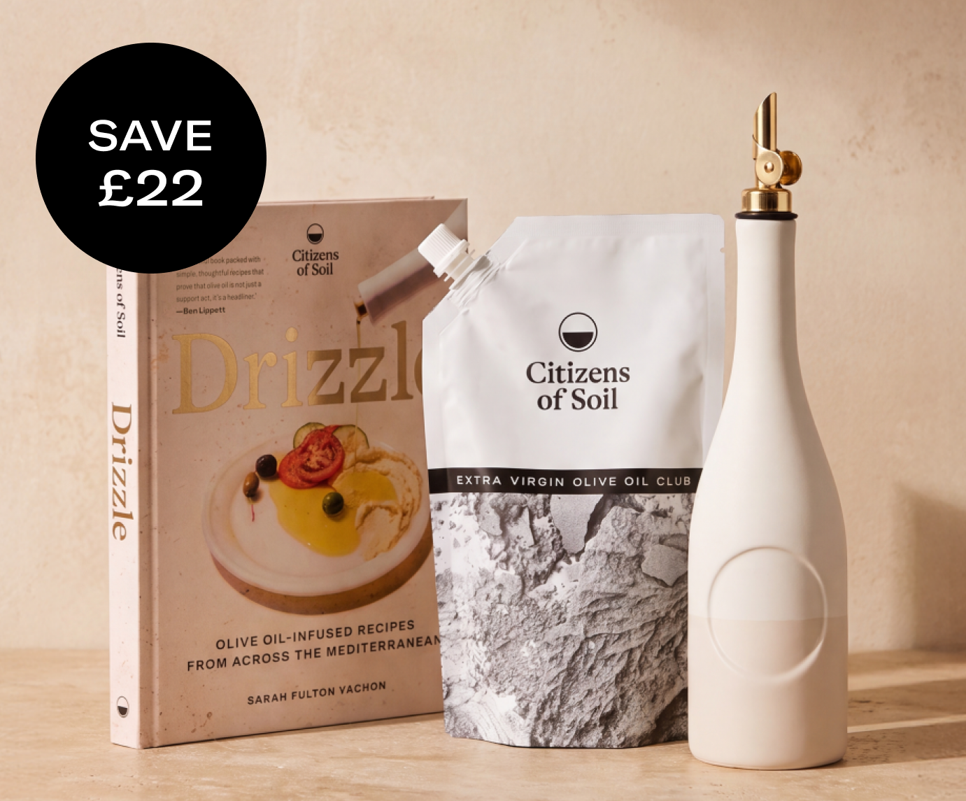 A cookbook titled 'Drizzle' next to a pouch of olive oil and a white dispenser bottle.