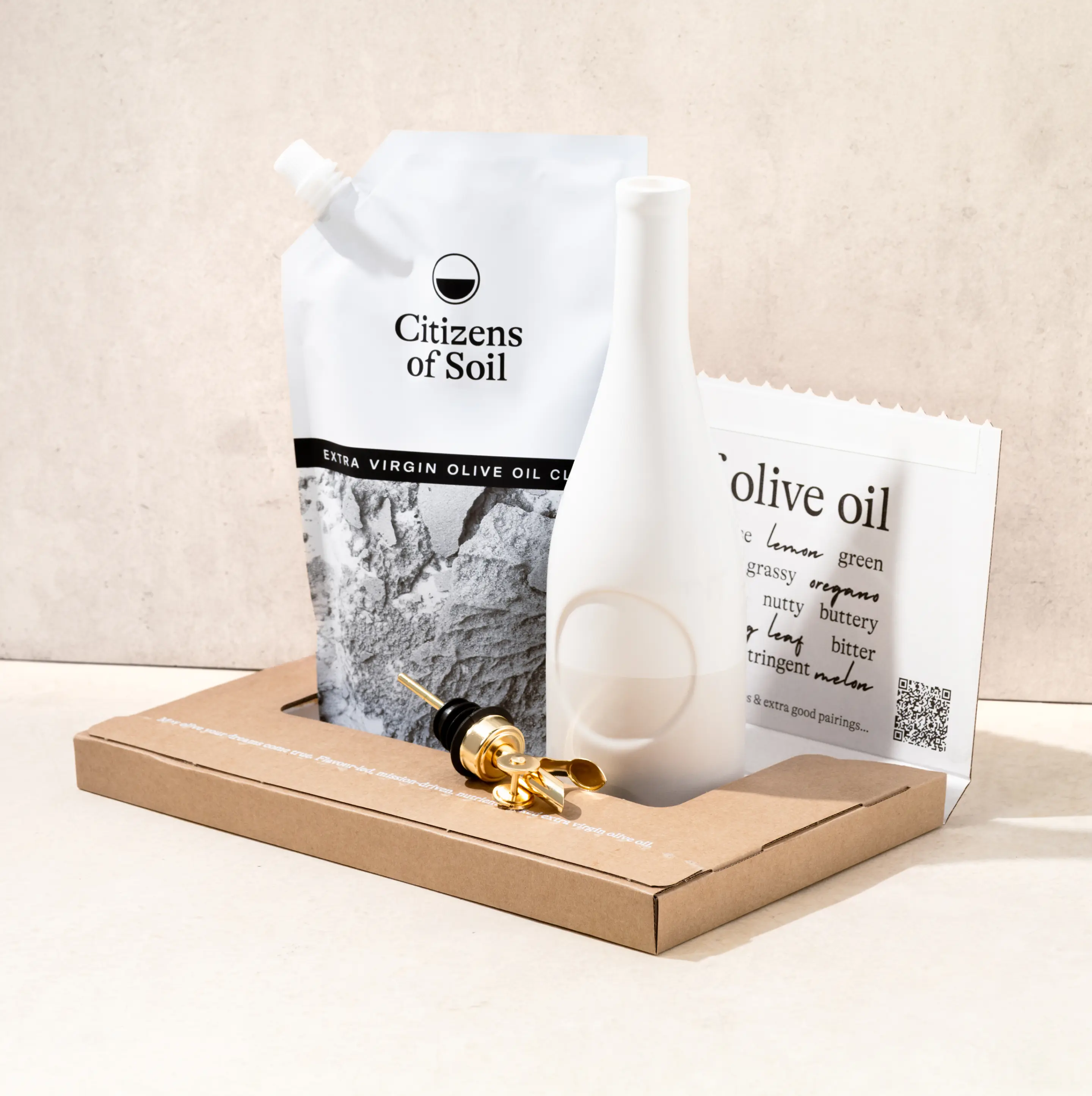 Olive oil packaging set with a pouch, bottle, and golden pourer on a cardboard tray.