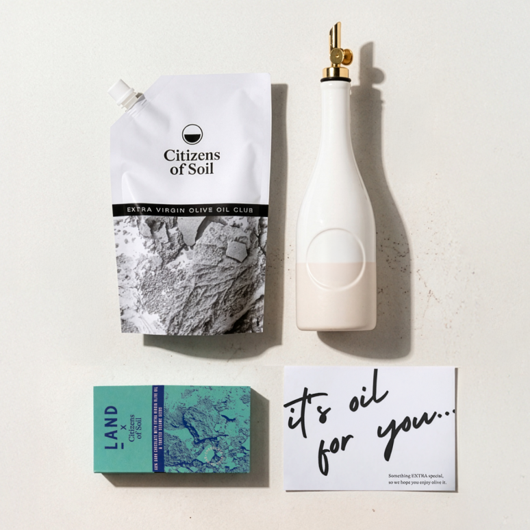 A cookbook titled 'Drizzle' next to a pouch of olive oil and a white dispenser bottle.