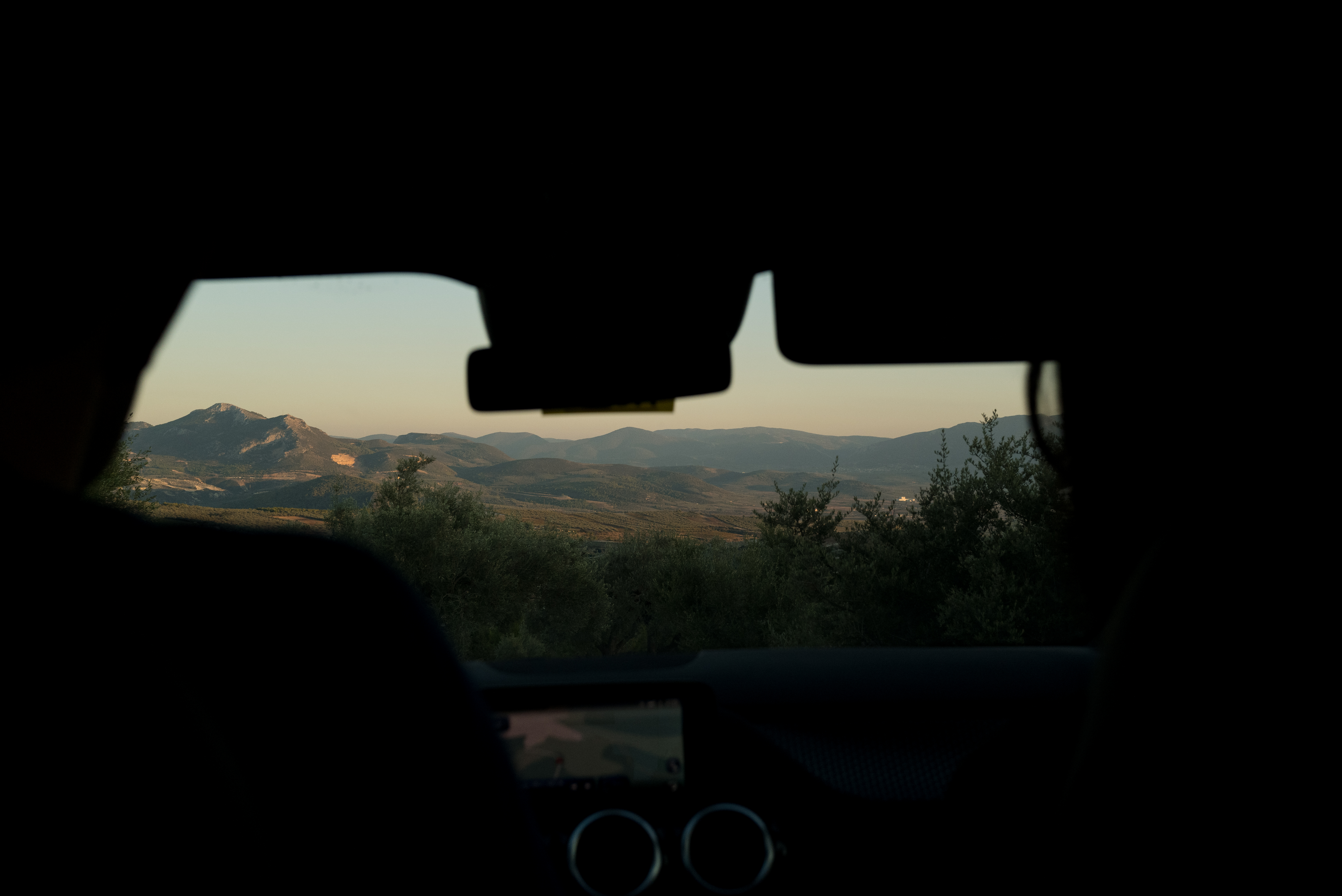 A view of rolling hills and mountains at dusk, seen from inside a silhouetted car.