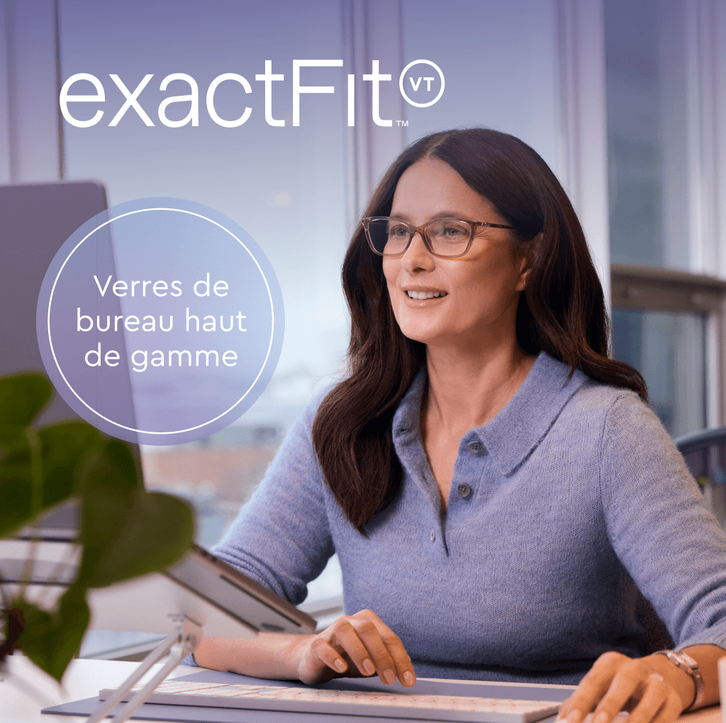 Une femme souriante portant des lunettes est assise à son bureau dans un environnement de bureau et utilise un ordinateur.