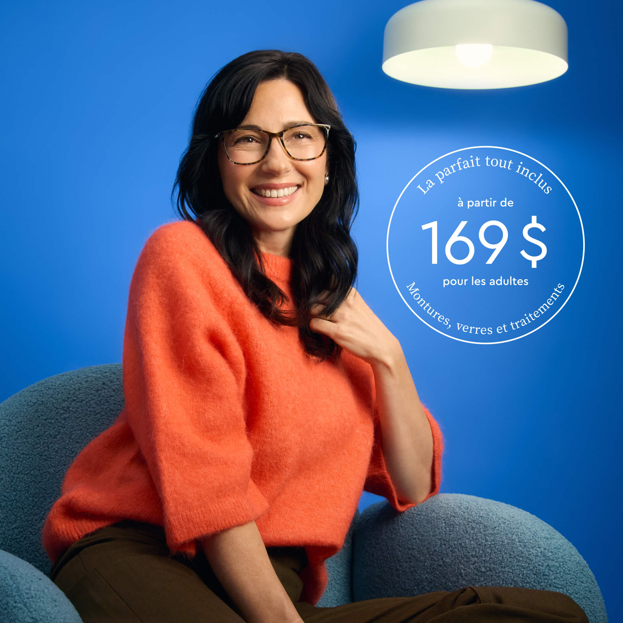 Femme portant des lunettes, vêtue d’un chandail orange, assise sur une chaise bleue, sur fond bleu.