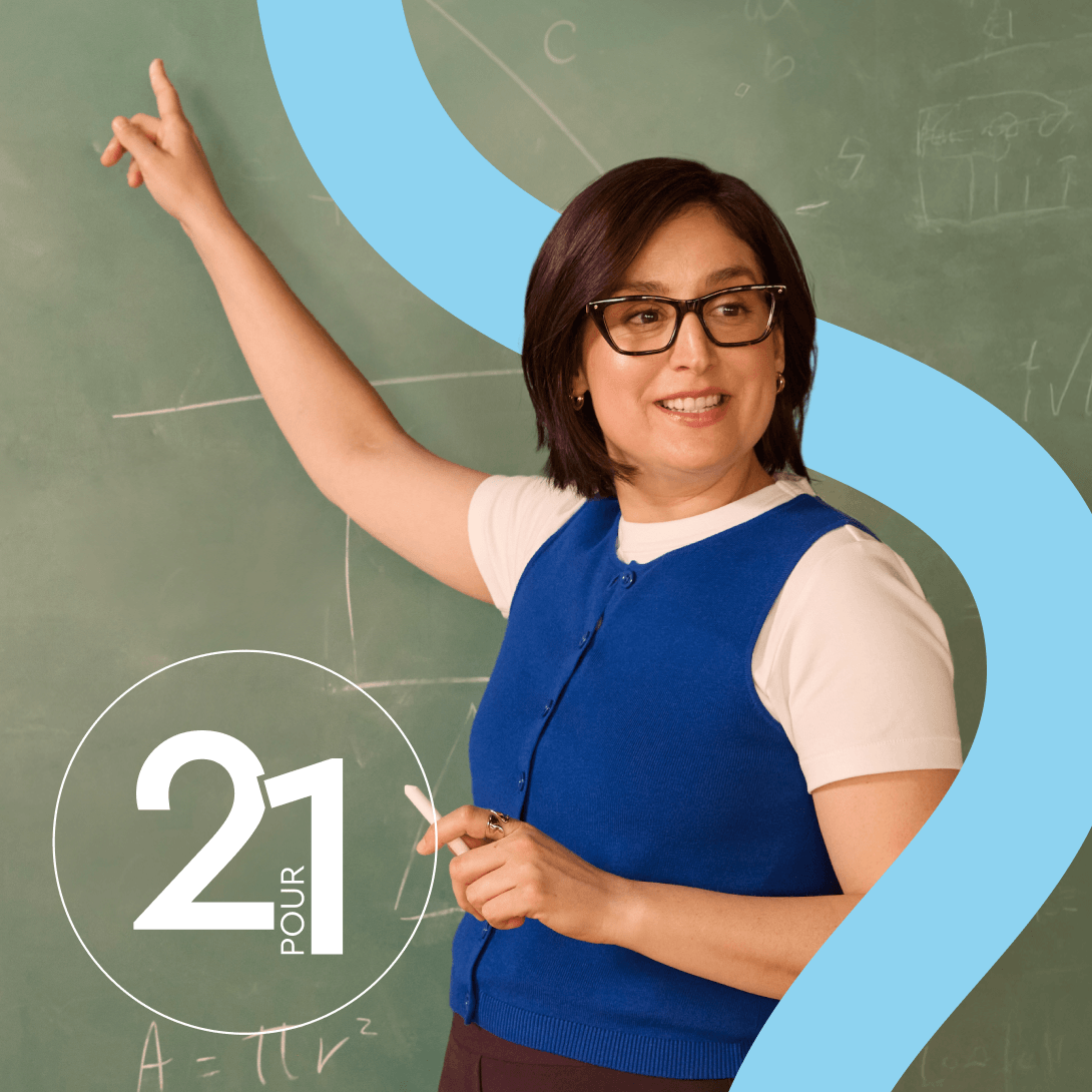 Enseignante souriante portant des lunettes, tenant une craie et pointant des équations sur un tableau vert.