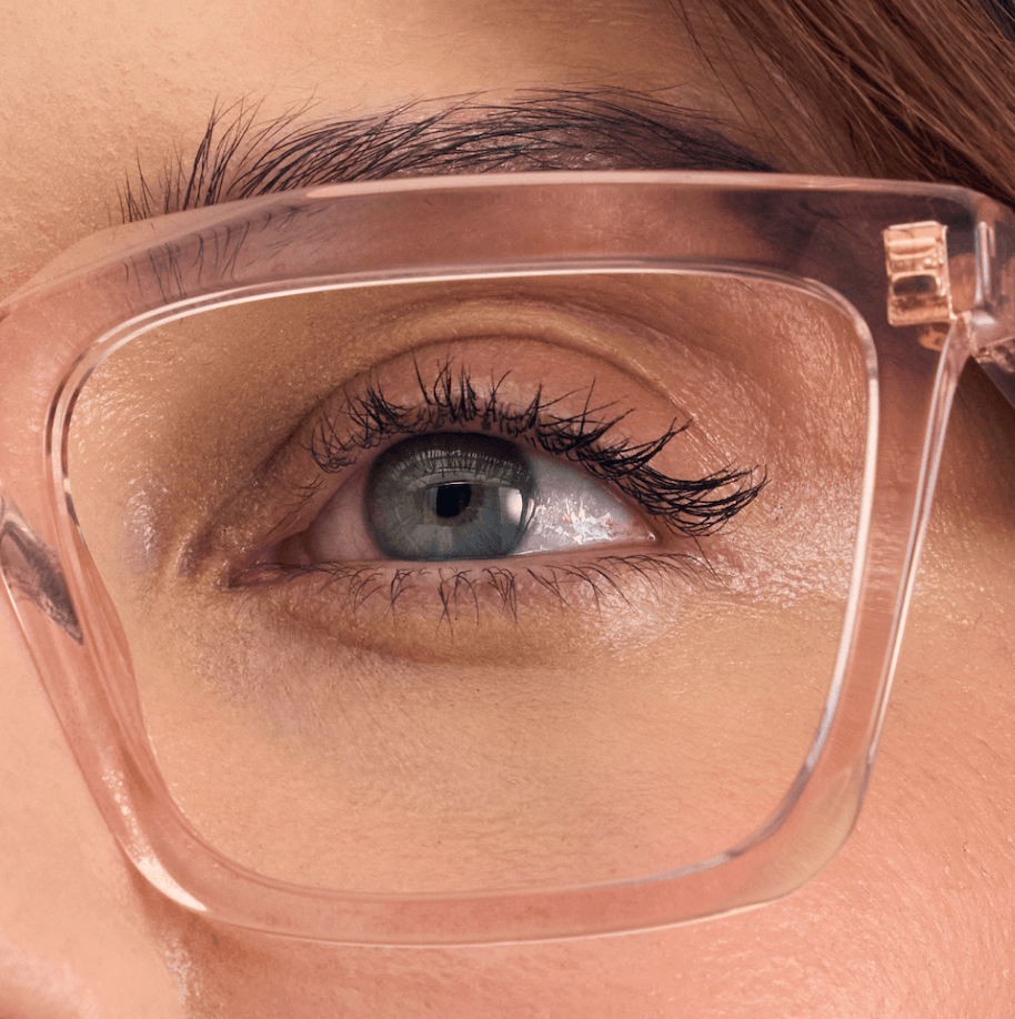 Gros plan sur un œil bleu-gris regardant à travers des lunettes à monture transparente.