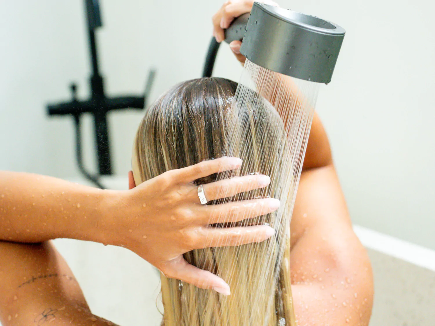 Person washing hair under a showerhead, hand touching wet hair.