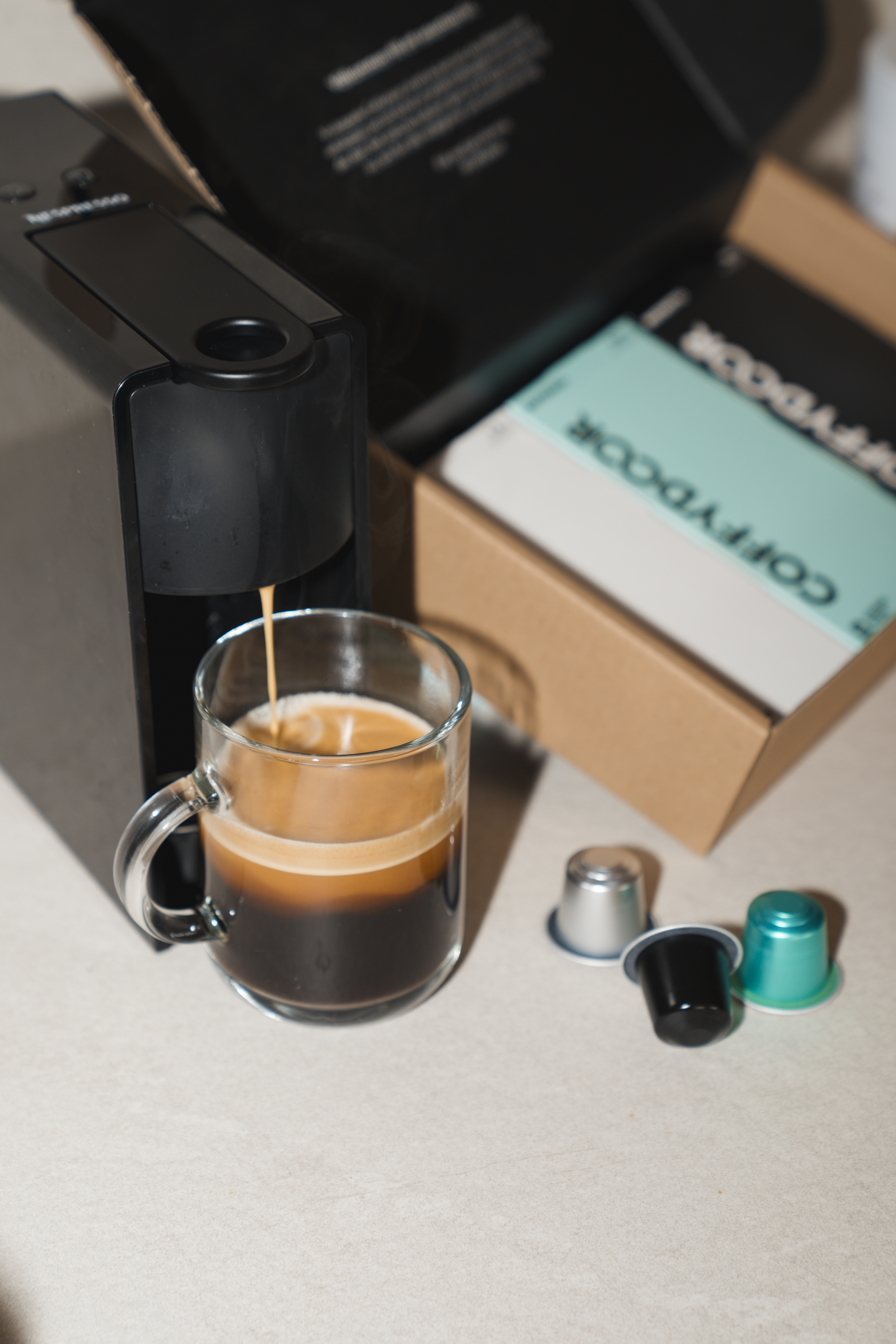 Coffee machine brewing espresso into a glass mug with capsules nearby.