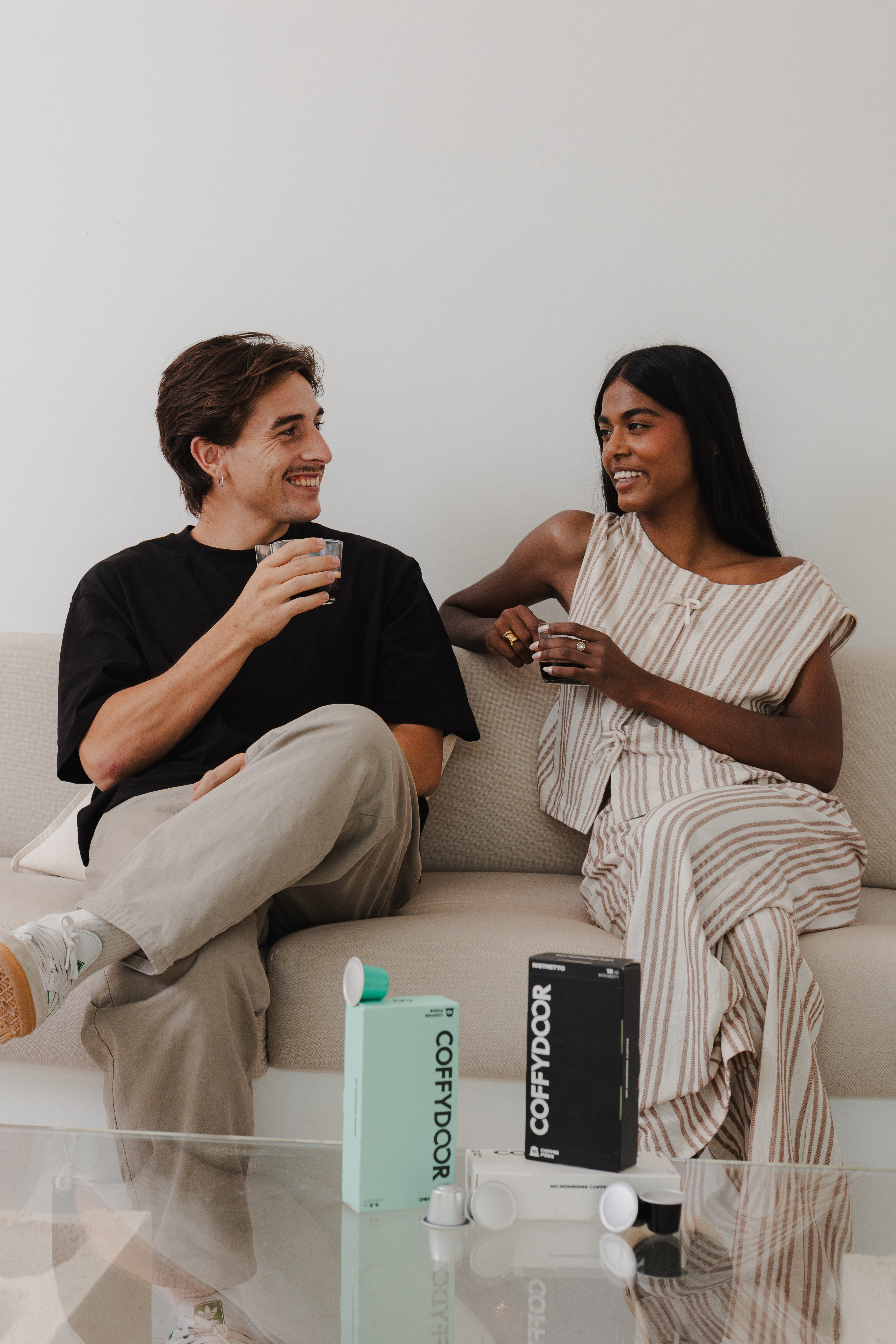 Two people sitting on a couch, smiling and holding drinks.